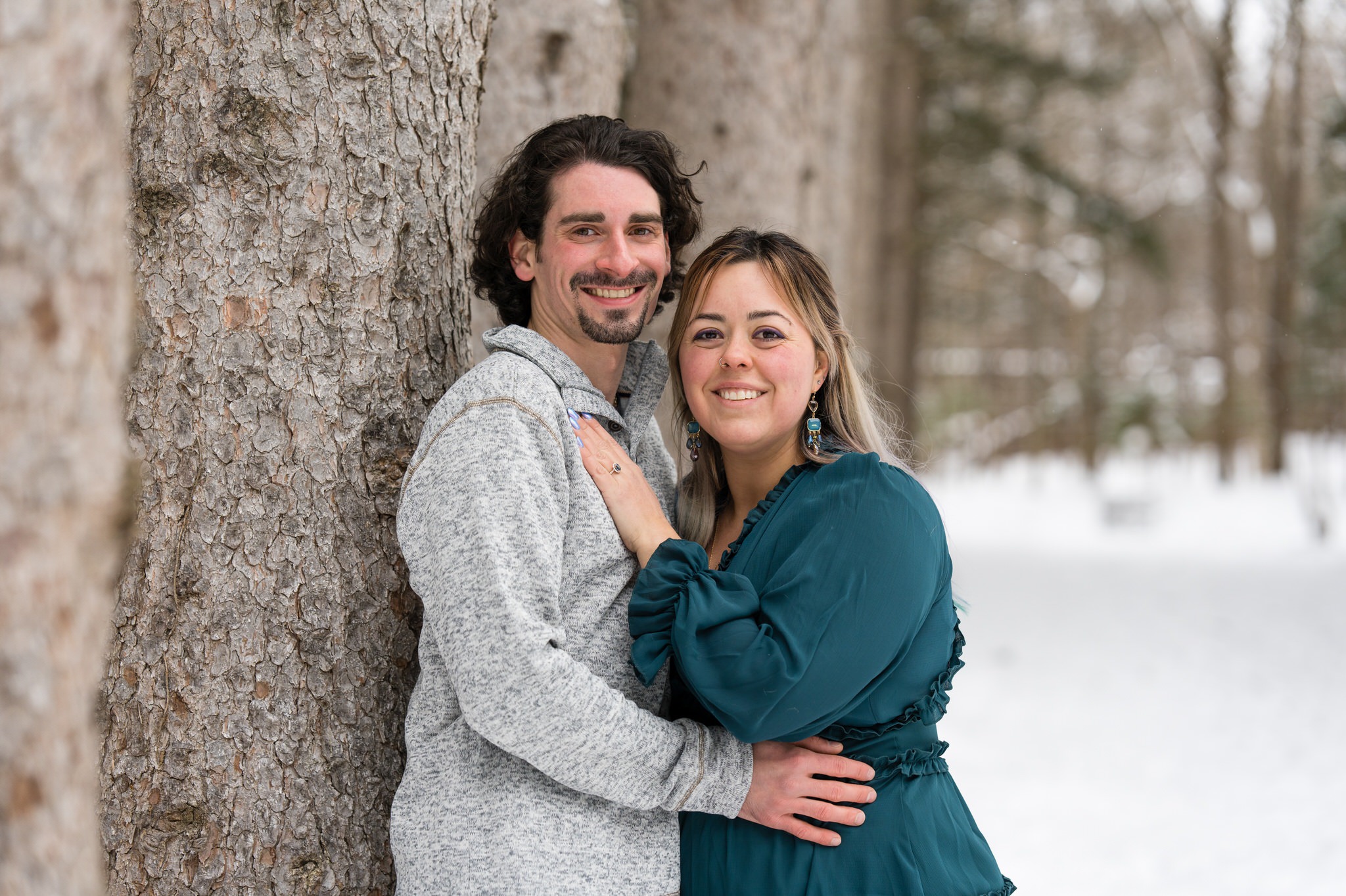 A couple pose with a tree in the snow for their winter engagement session at Stony Creek. 