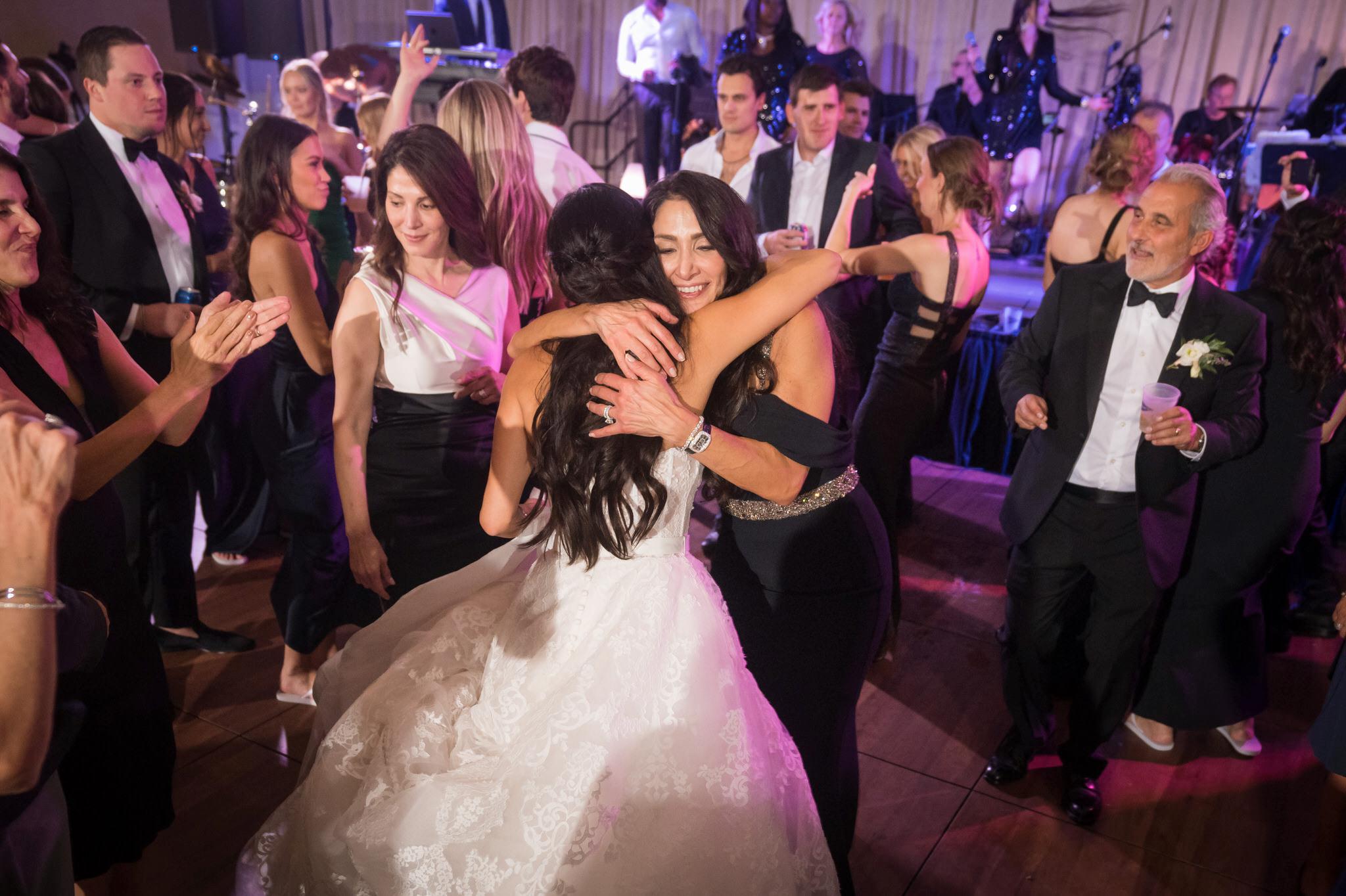 A mom hugs the bride one the dancefloor at a wedding at Bay Harbor. 