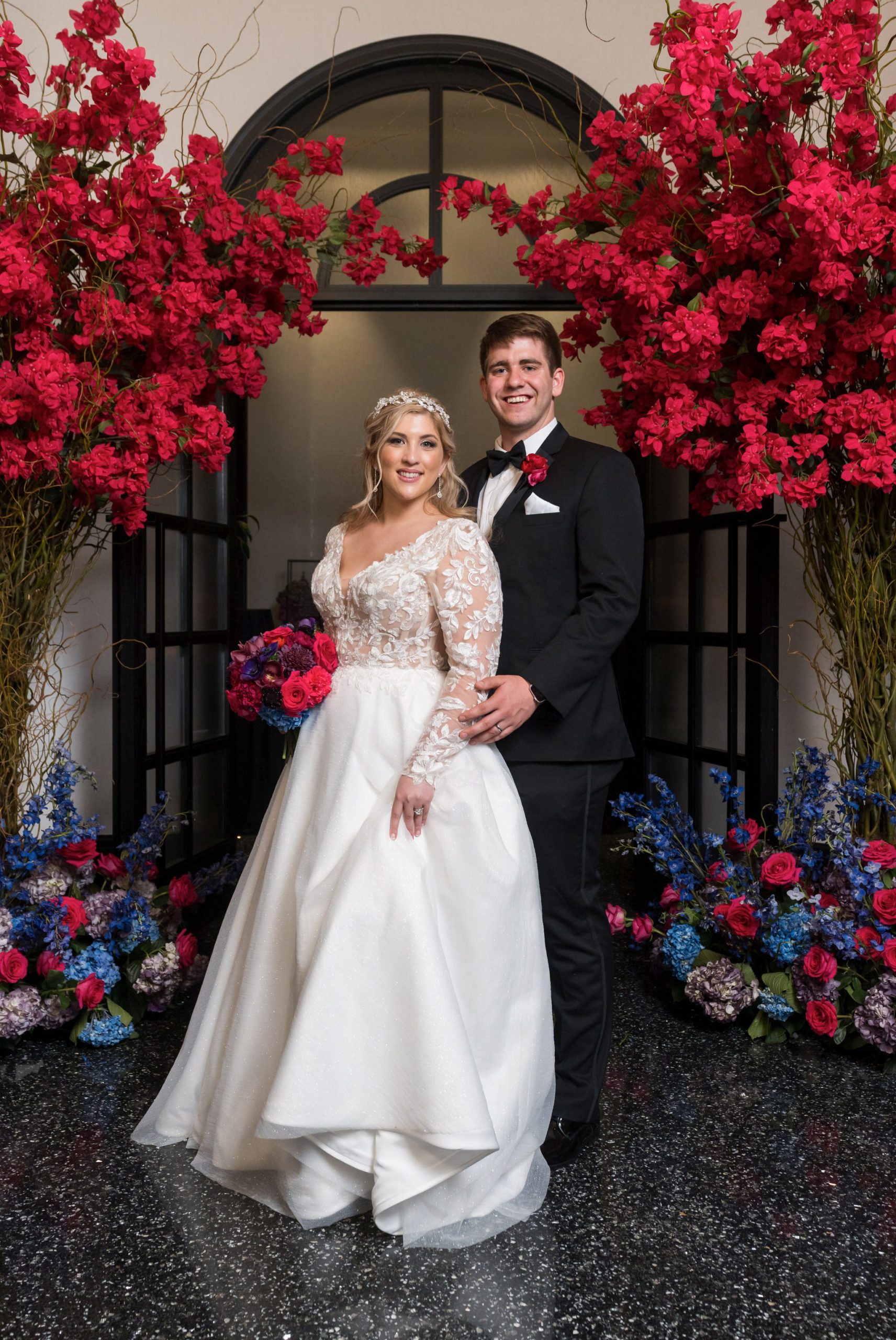 A bride and groom pose under a colorful archway to the entrance of their Daxton Hotel wedding.  