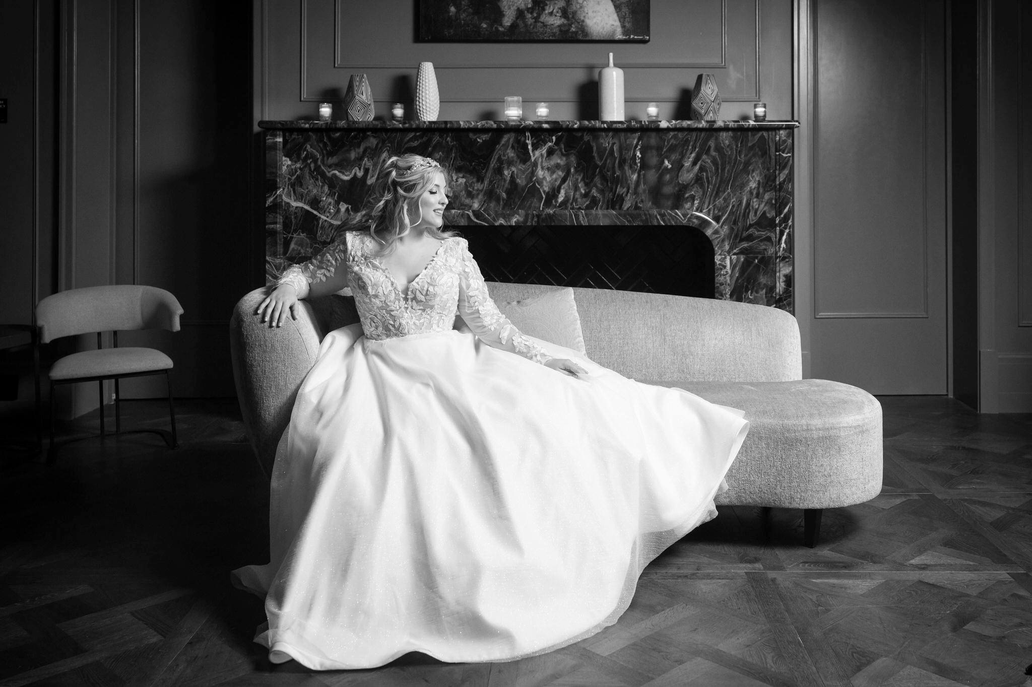 A bride sitting on a chaise lounge poses in a formal fashion at her Daxton Hotel wedding.  