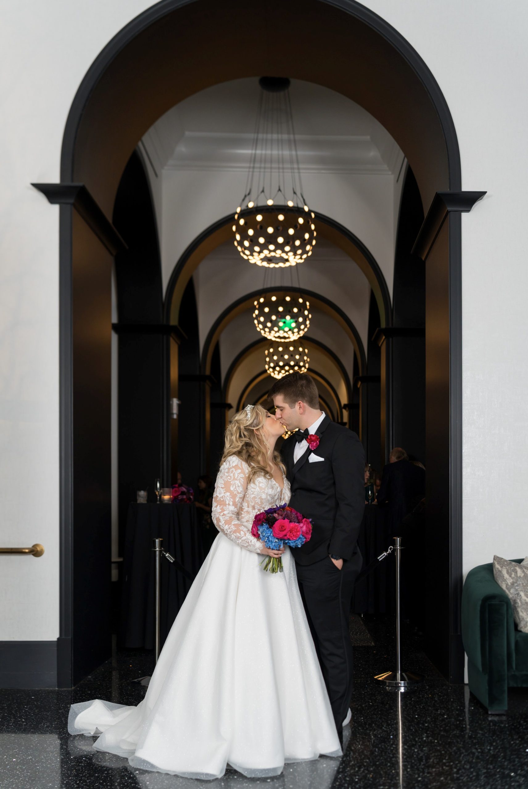 A groom kisses the bride with golden chandeliers behind them at their Daxton Hotel wedding.  