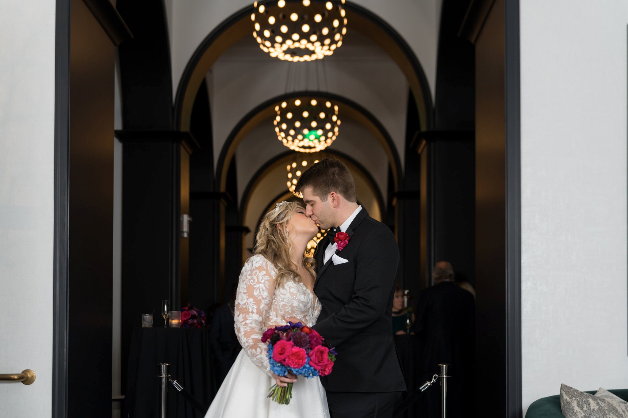 A groom kisses the bride with golden chandeliers behind them at their Daxton Hotel wedding.  