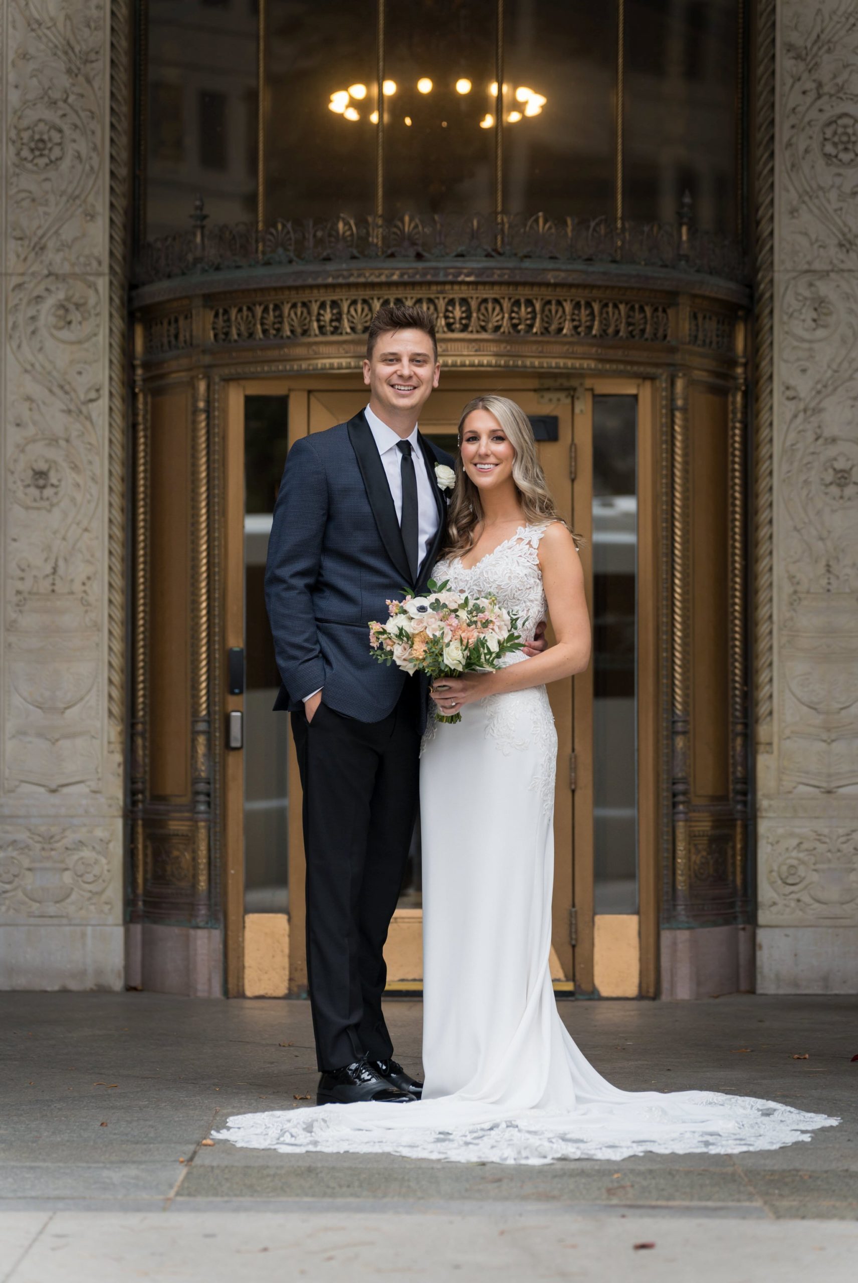Newlyweds pose in front of a brass doorway at the Cadillac Place apartments.  