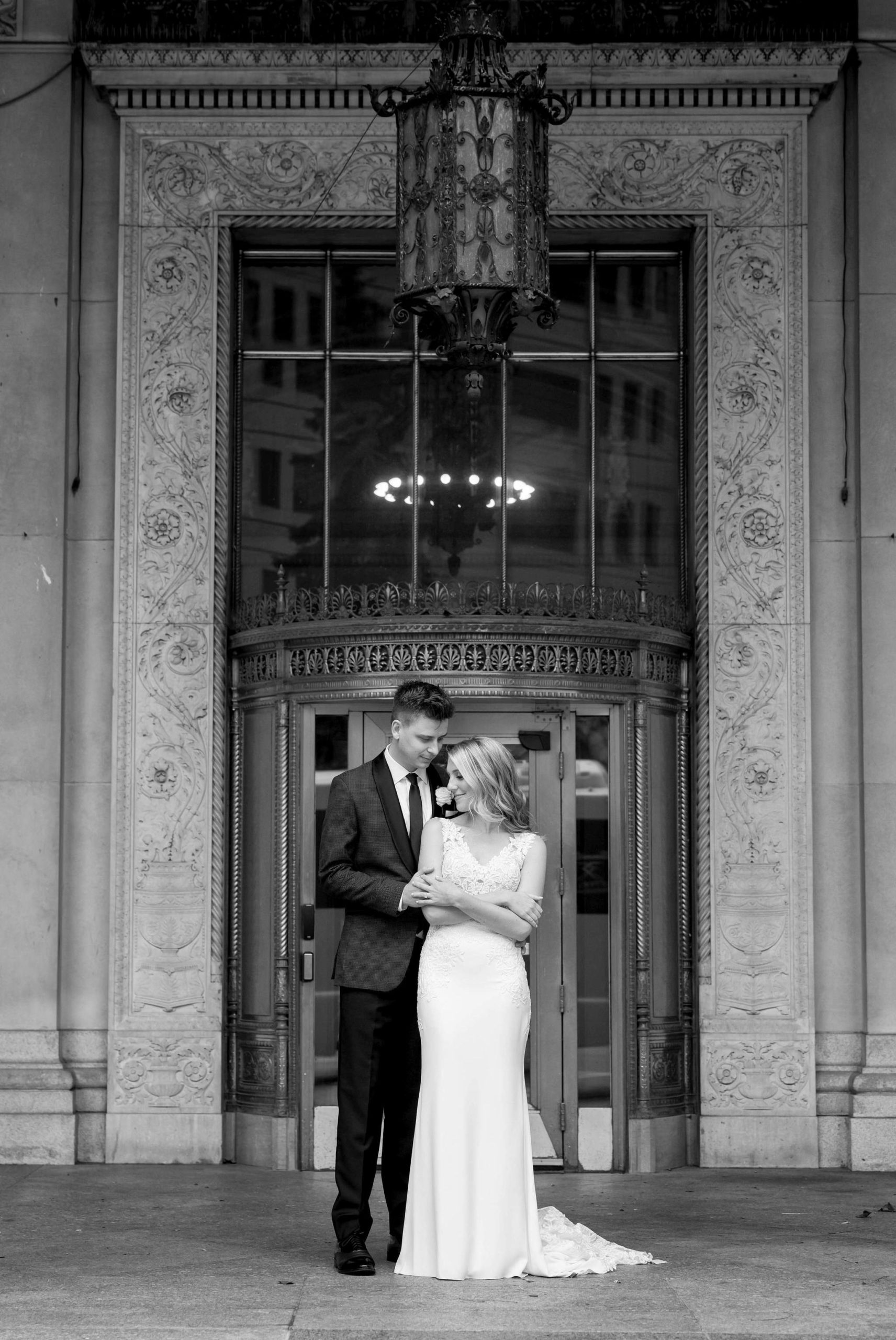 Newlyweds pose in front of a brass doorway at the Cadillac Place apartments.  