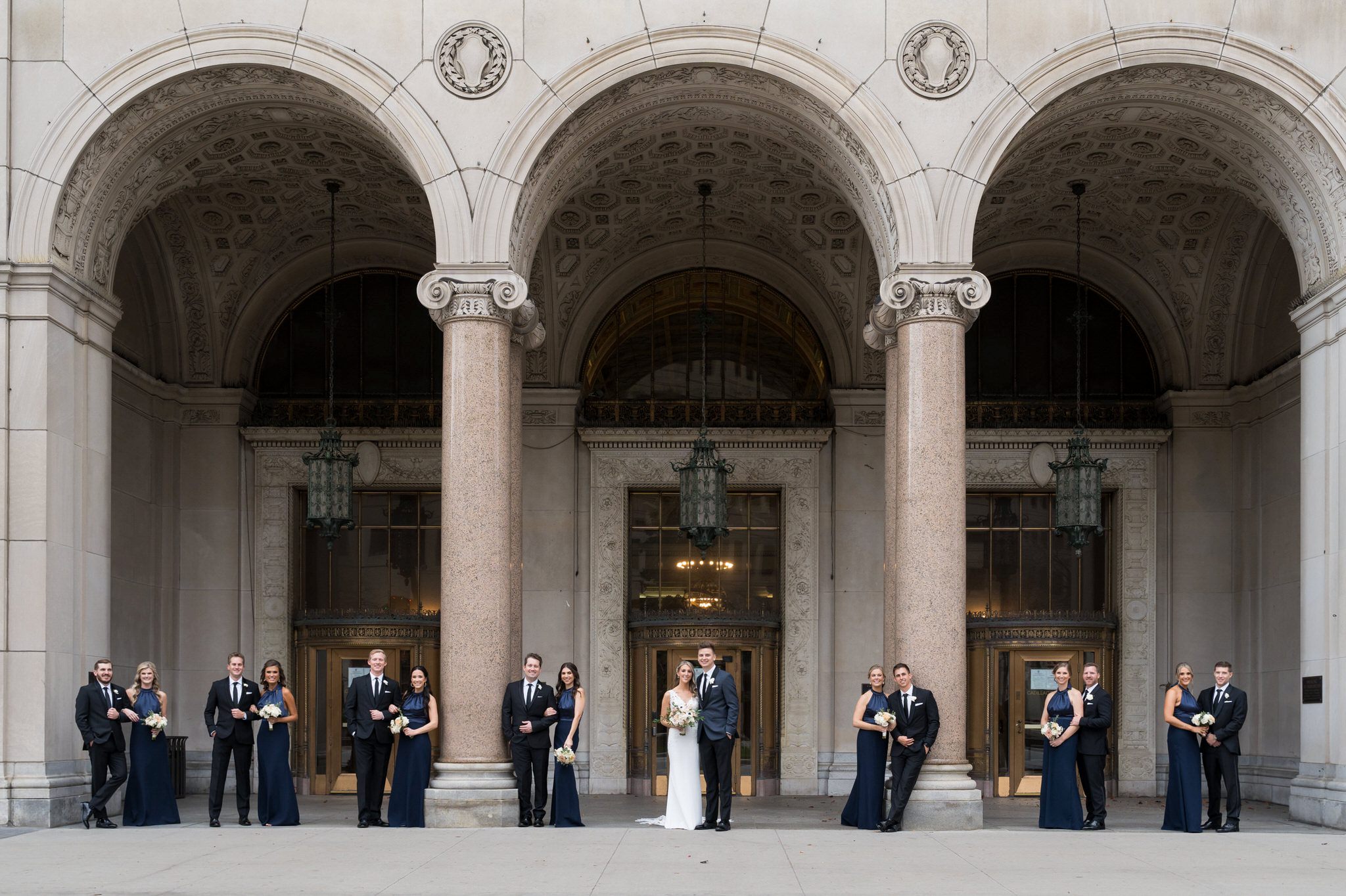 A bridal party poses in front of three giant arches at the Cadillac Place apartments in Detroit, MI.   
