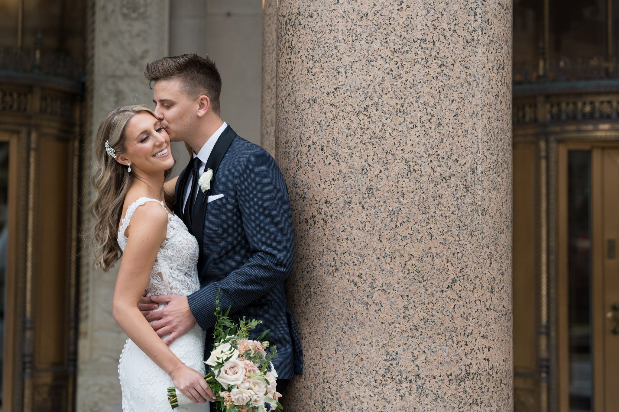 The groom kisses the temple of his  bride outside of the Cadillac Place Apartments. 