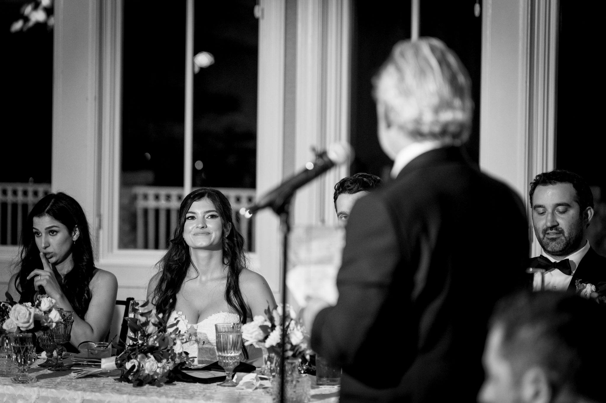 A bride looks at her father-in-law while he gives a wedding toast.