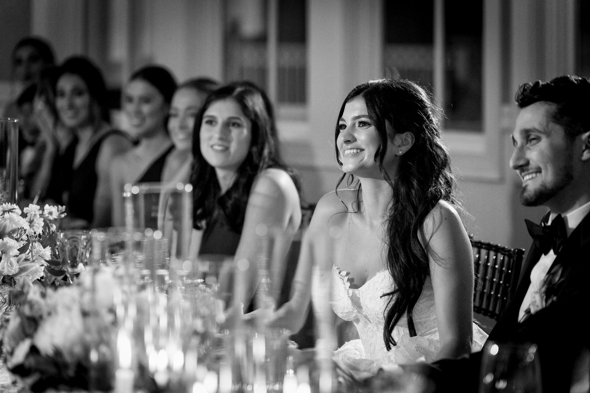 A bride smiles and looks on during toasts at their wedding at Bay Harbor.  