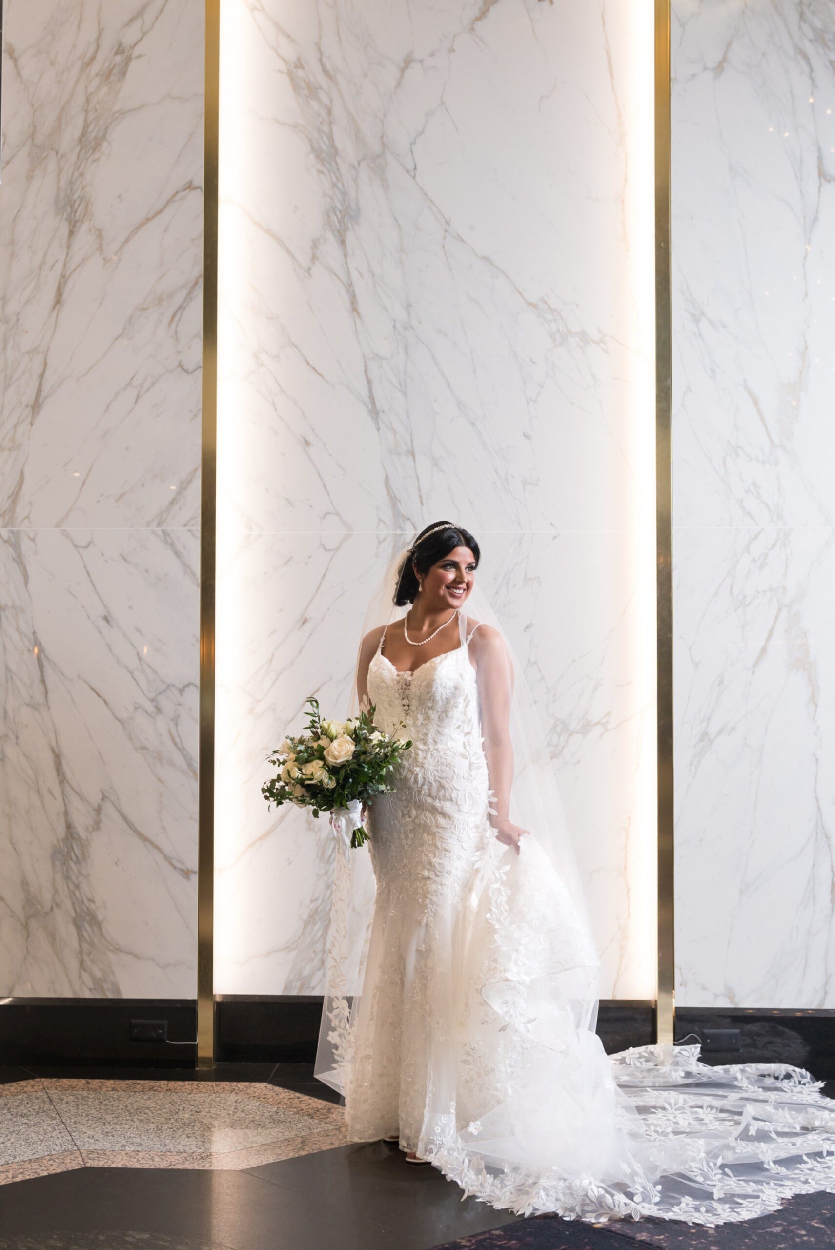 A bride holds her dress and bouquet during a portrait in the lobby of the Atheneum Hotel. 