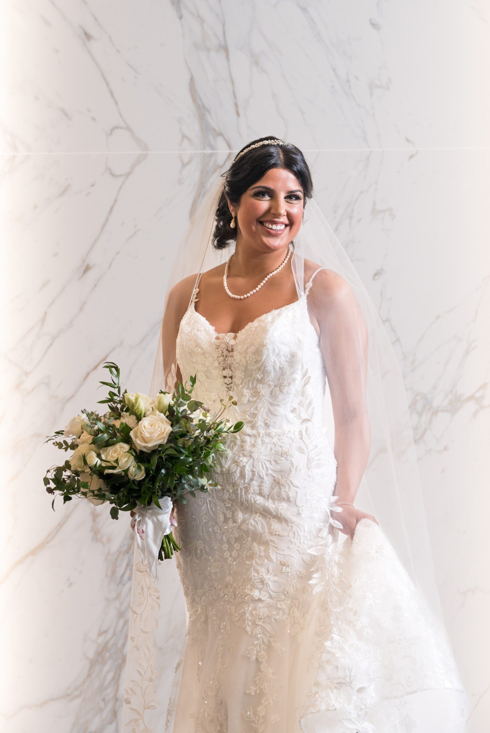 A bride holds her dress and bouquet during a portrait in the lobby of the Atheneum Hotel. 