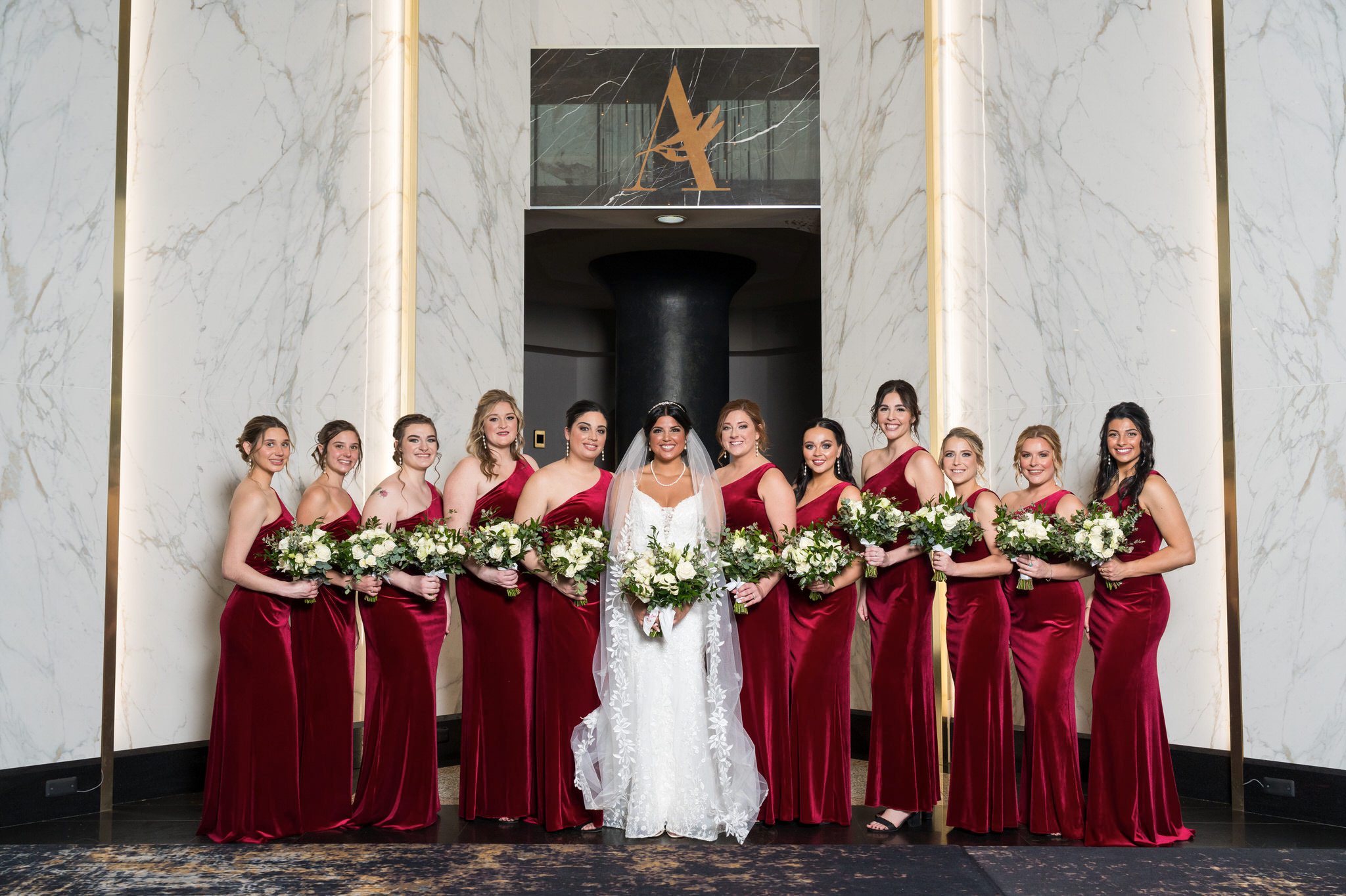 Bridesmaids wearing ruby red dresses pose for a portrait in the lobby of the Atheneum Hotel. 