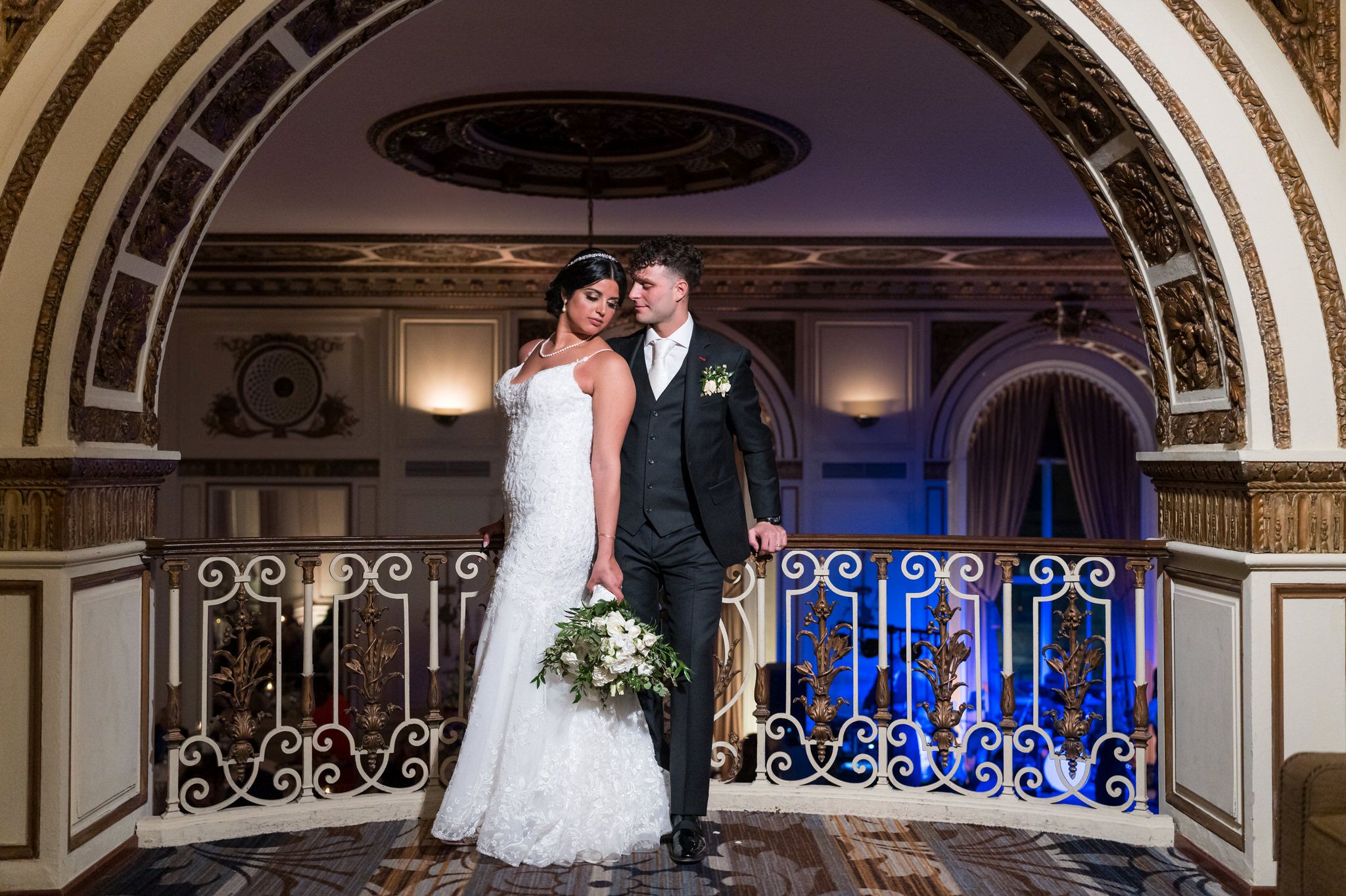 A bride and groom pose, resting on a balcony railing, at their Colony Club Detroit wedding. 
