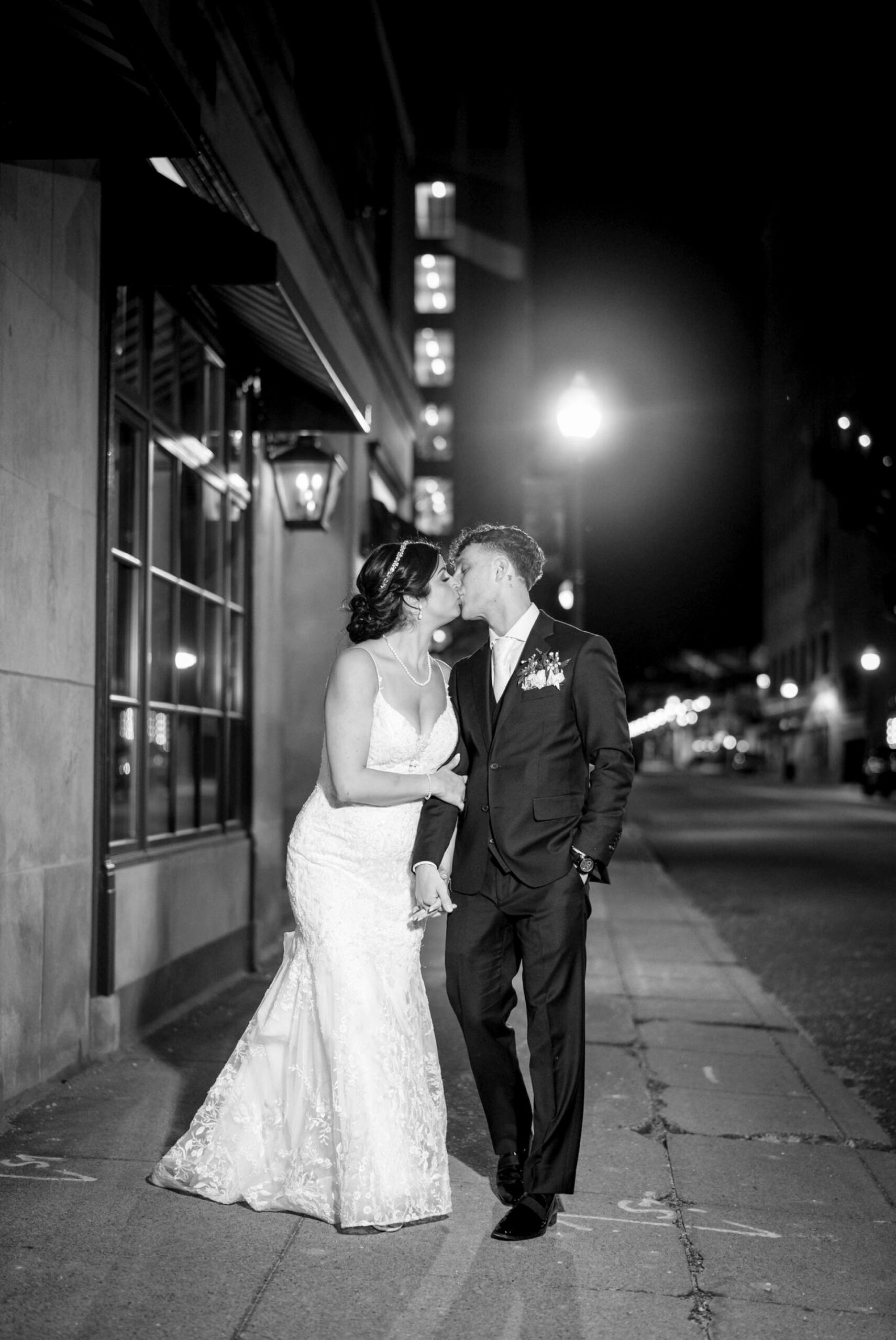 A black and white image of a bride and groom kissing outside of their Colony Club Detroit wedding at night. 