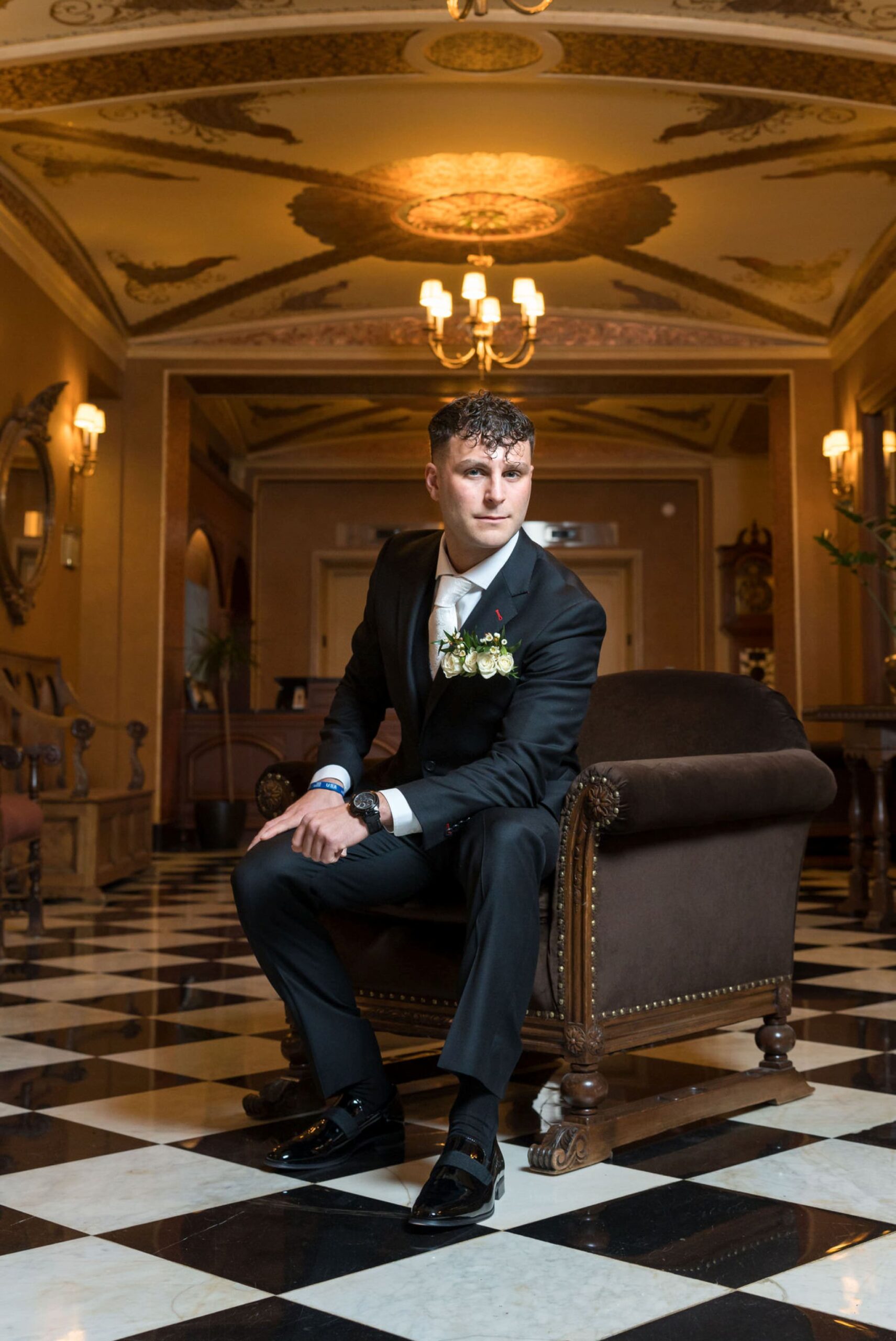 A groom sits in a chair and poses for a portrait on his Colony Club Detroit wedding day. 