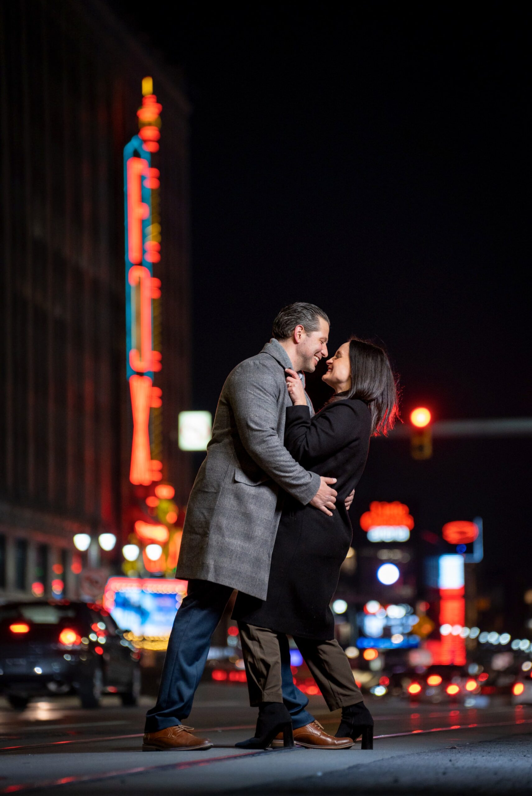 An engaged couple embrace and look at each other on Woodward Ave in Detroit with the Fox Theatre in the background. 