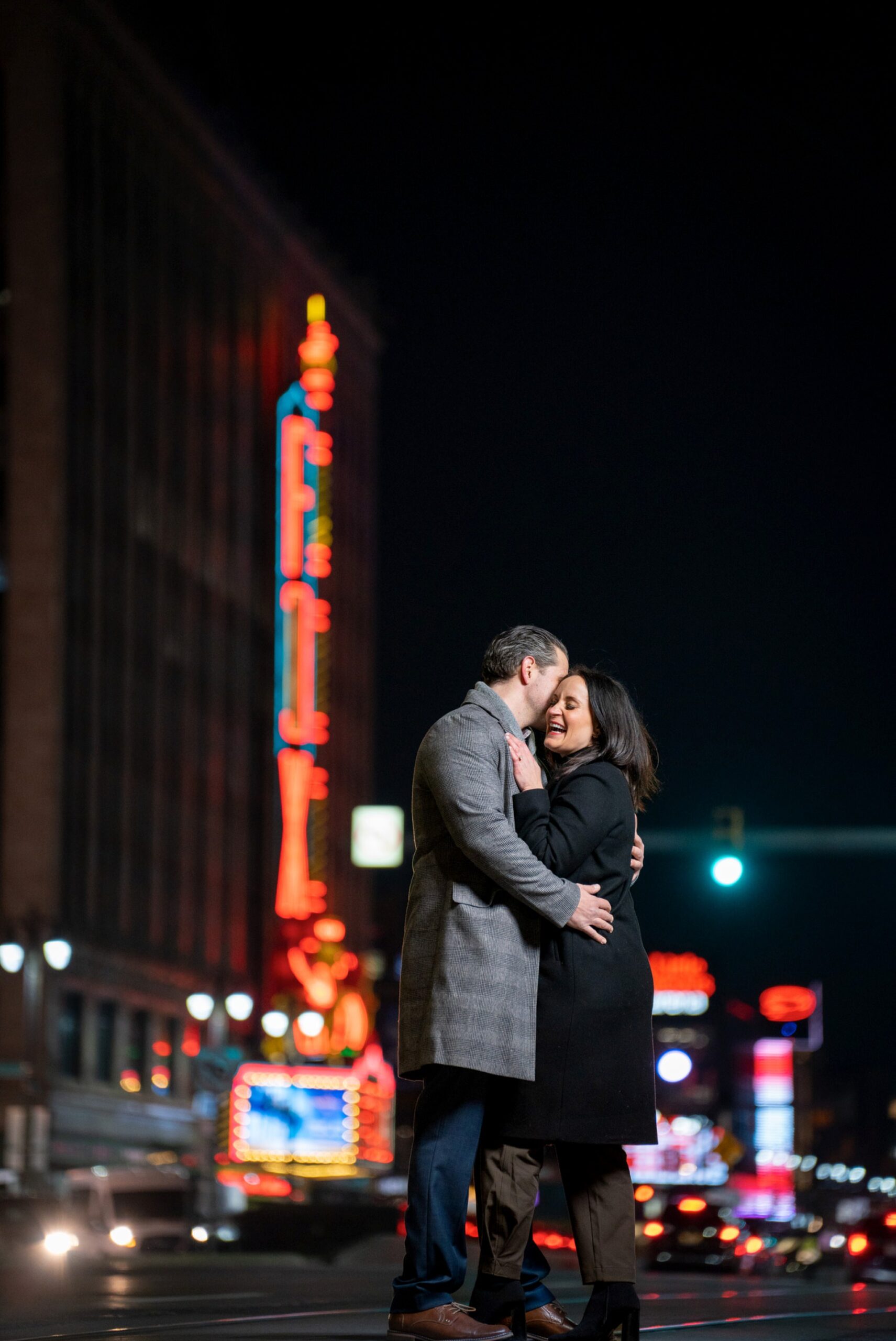 An engaged couple laughs on Woodward with the Fox Theatre in the background. 