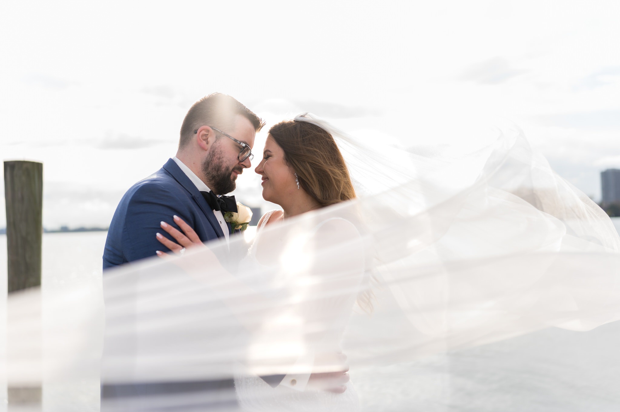 Bride and groom kiss at Detroit Yacht Club wedding with veil blowing in front of them.