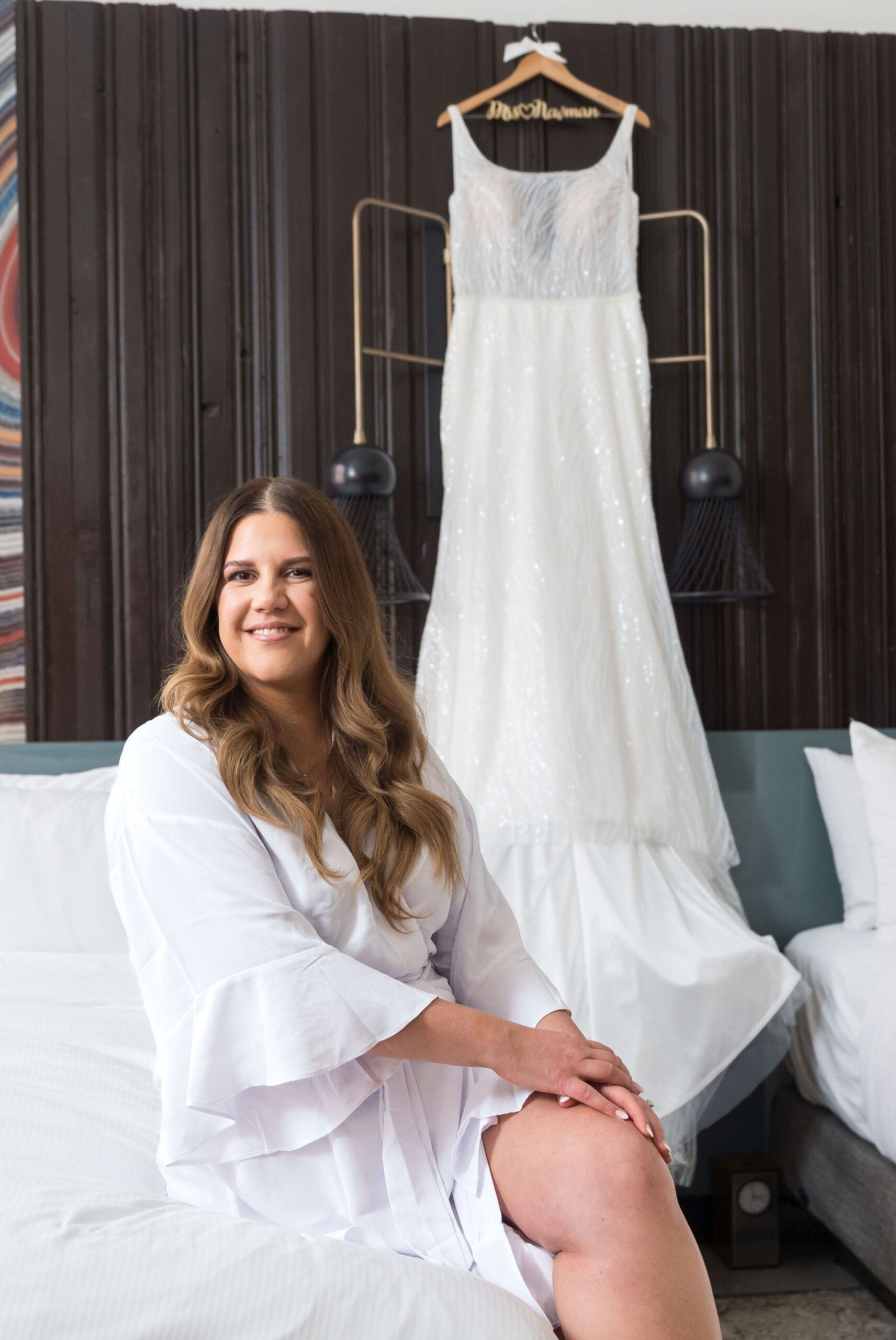 A bride sits on a bed with her dress in the background at the Foundation Hotel.