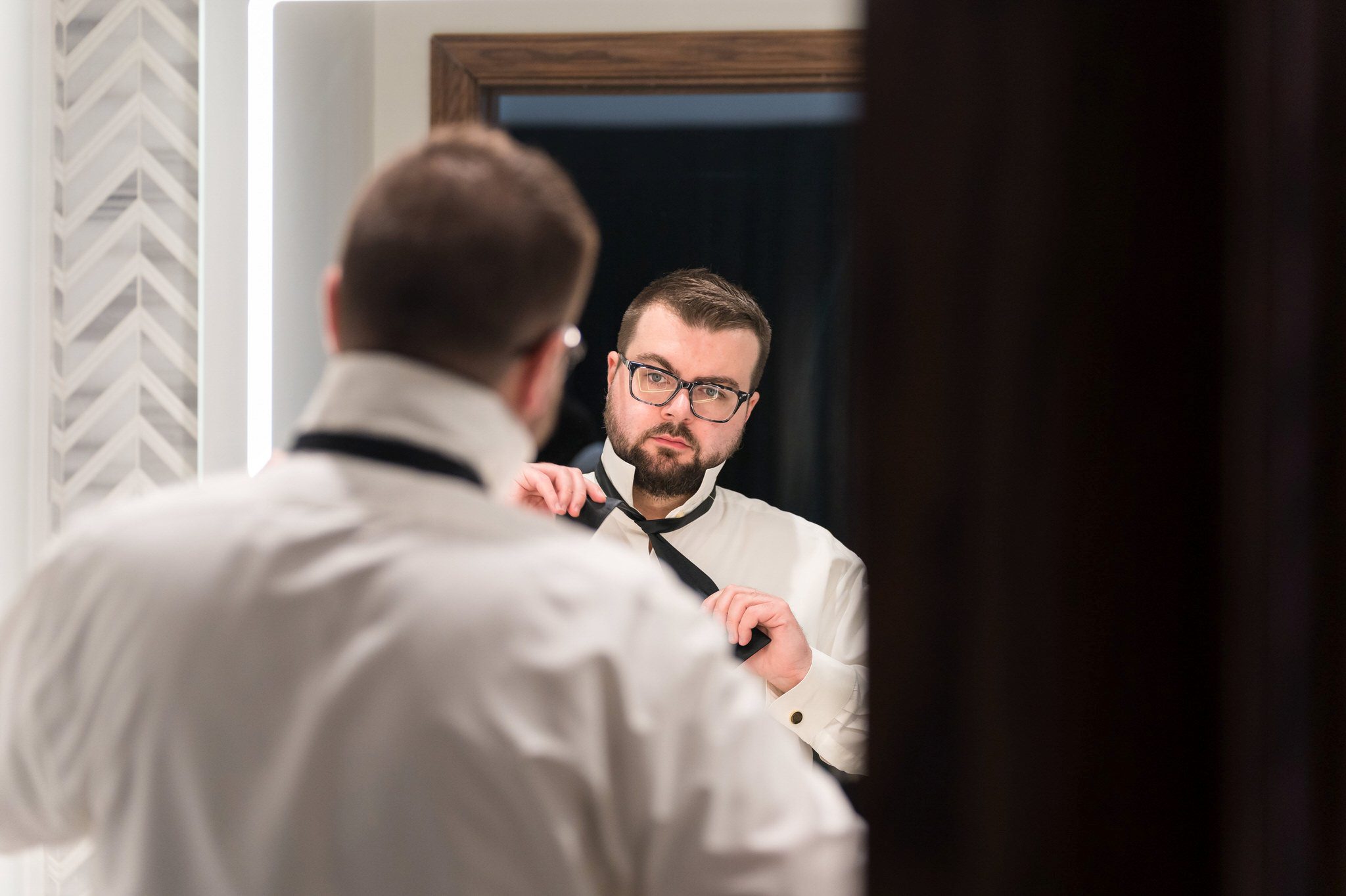 A groom ties his bowtie while looking in the mirror at the Foundation Hotel. 