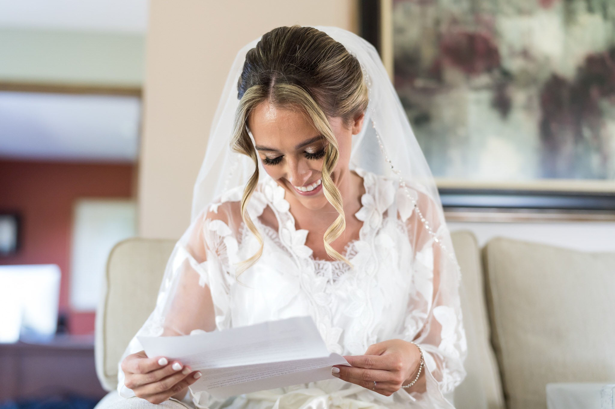 A bride smiles as she reads a letter from her husband on her wedding day. 