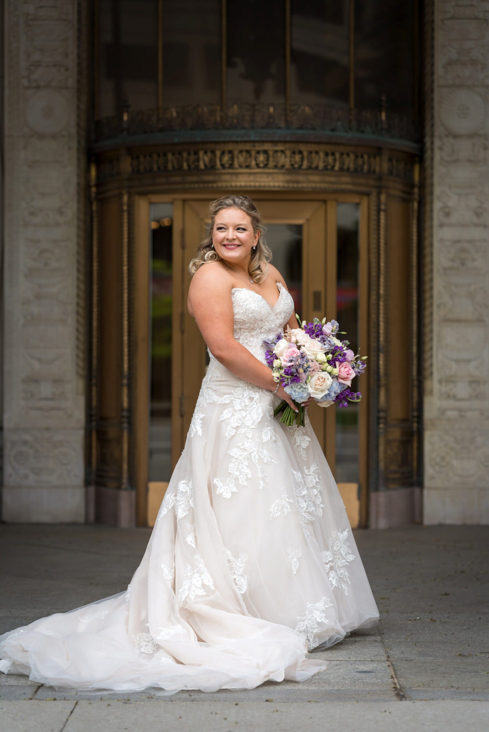 A bride looks over her shoulder in front of the Cadillac Place Apartments on her wedding day.  