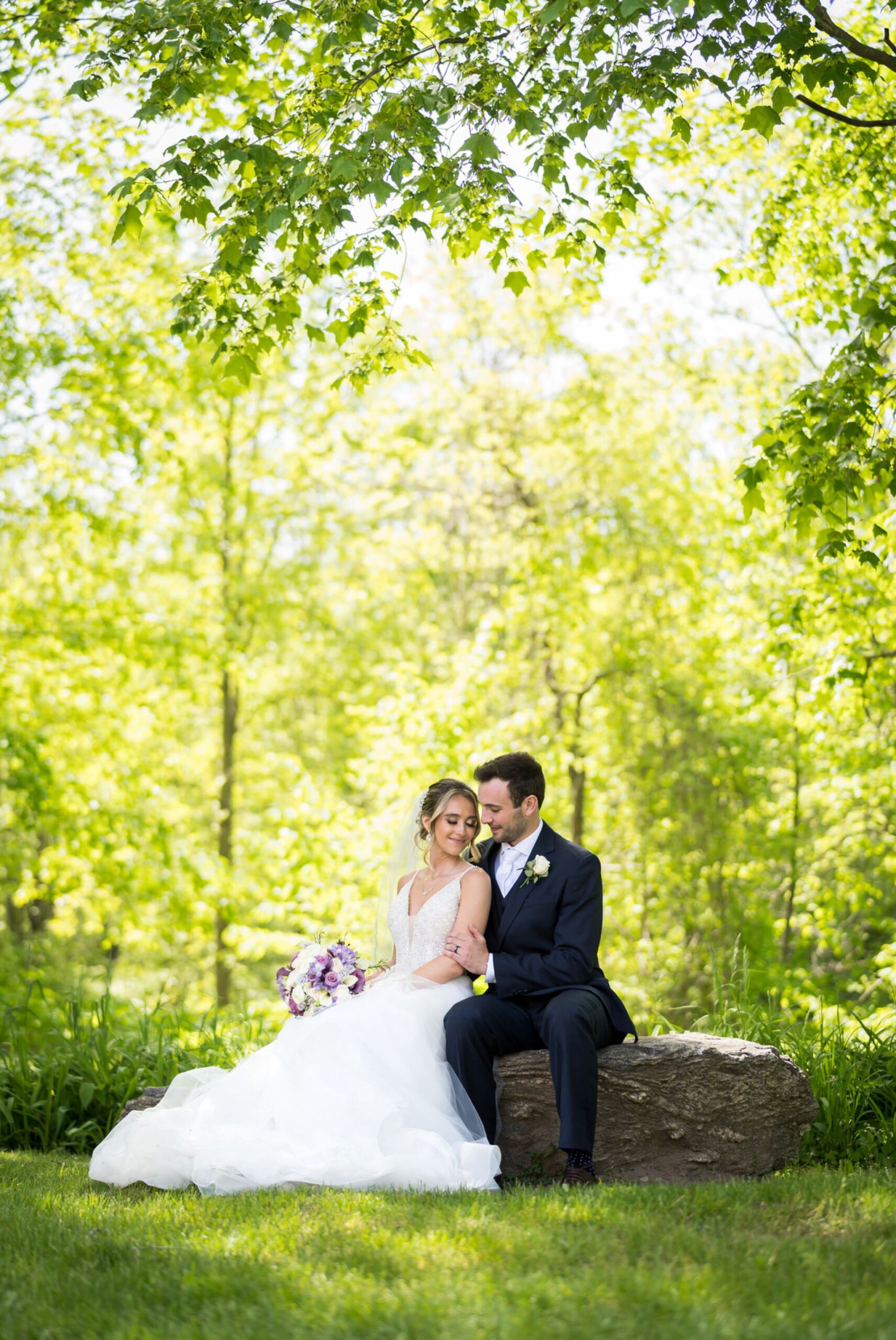 A bride and groom sit on a rock at their wedding at Van Hoosen Museum. 