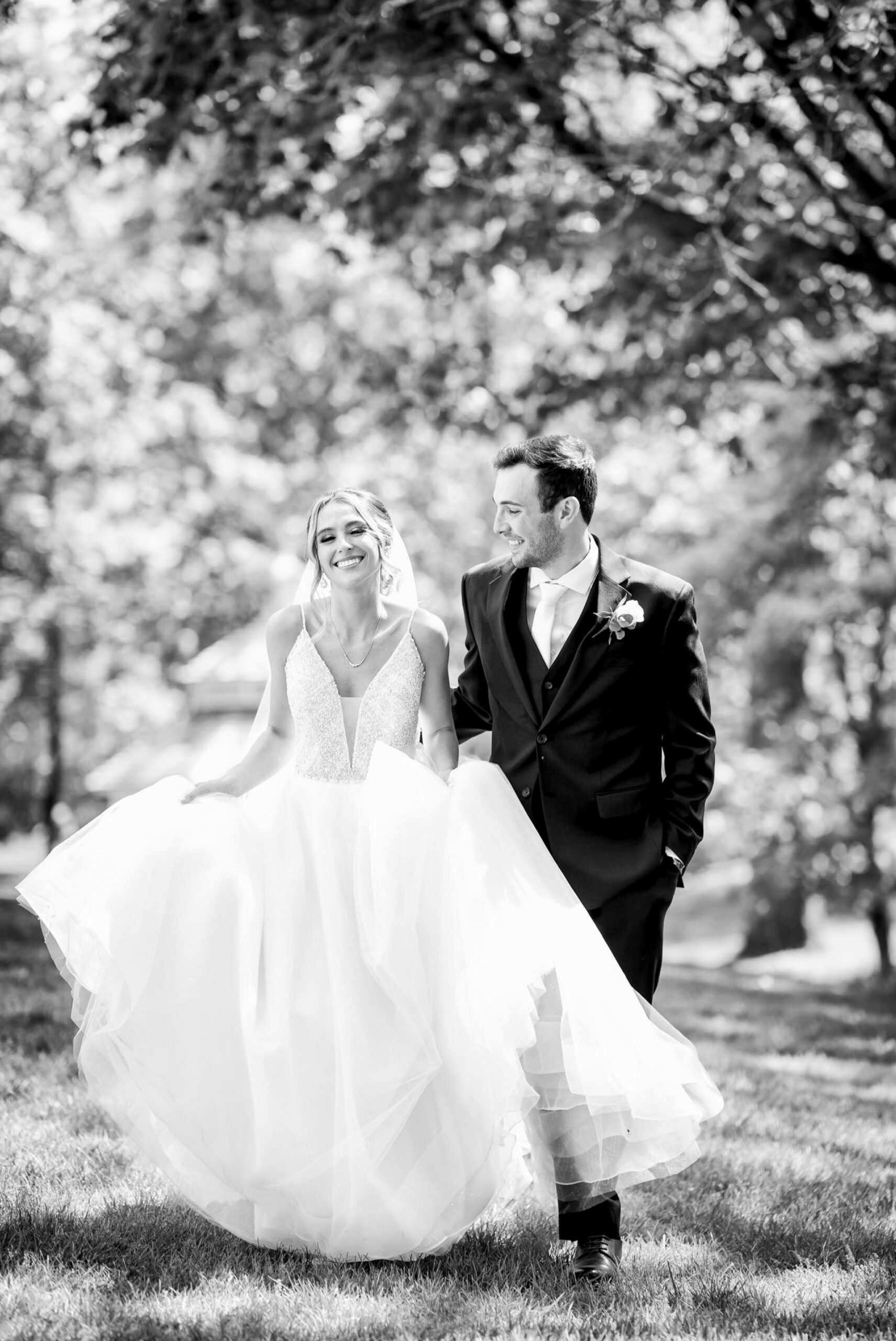 Carrying her dress, a bride laughs as she walks with her husband on her wedding day.  