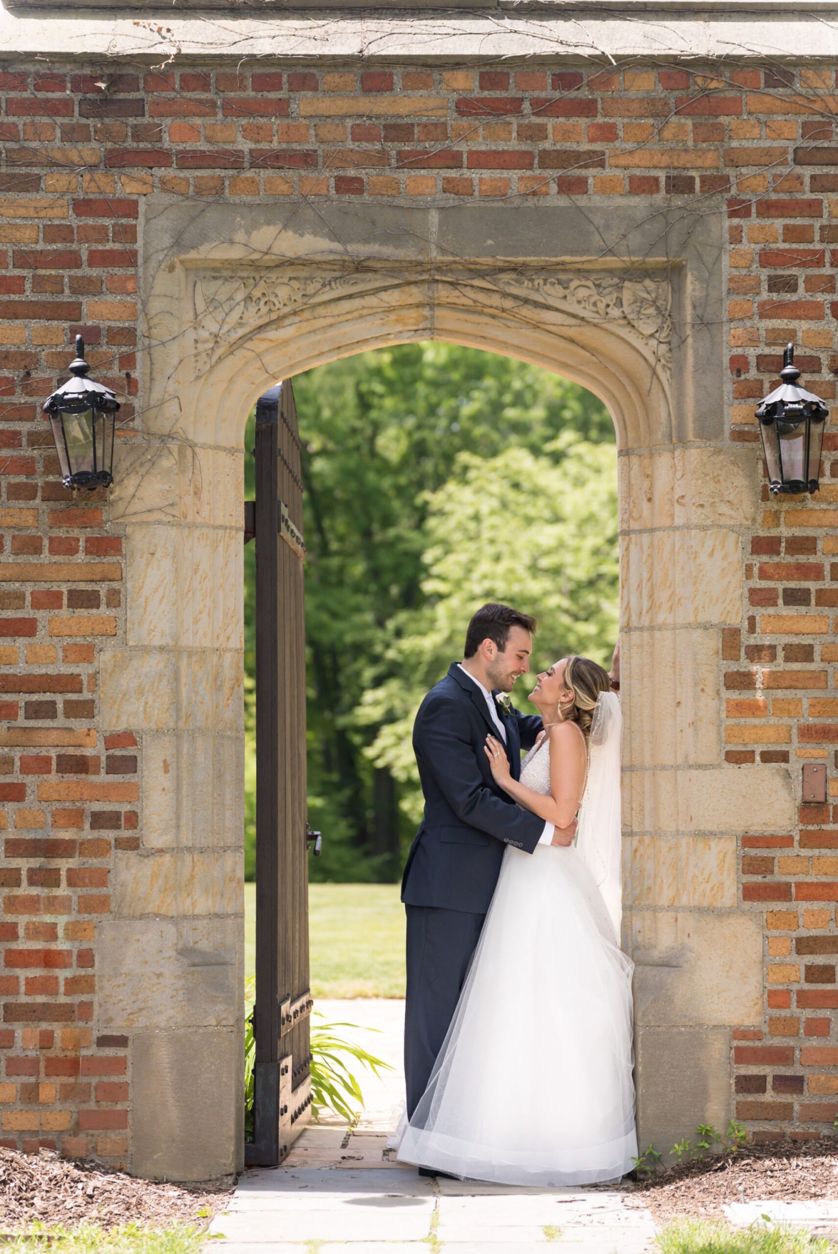 A bride and groom pose and almost kiss in an archway at their wedding at Meadowbrook Hall.  