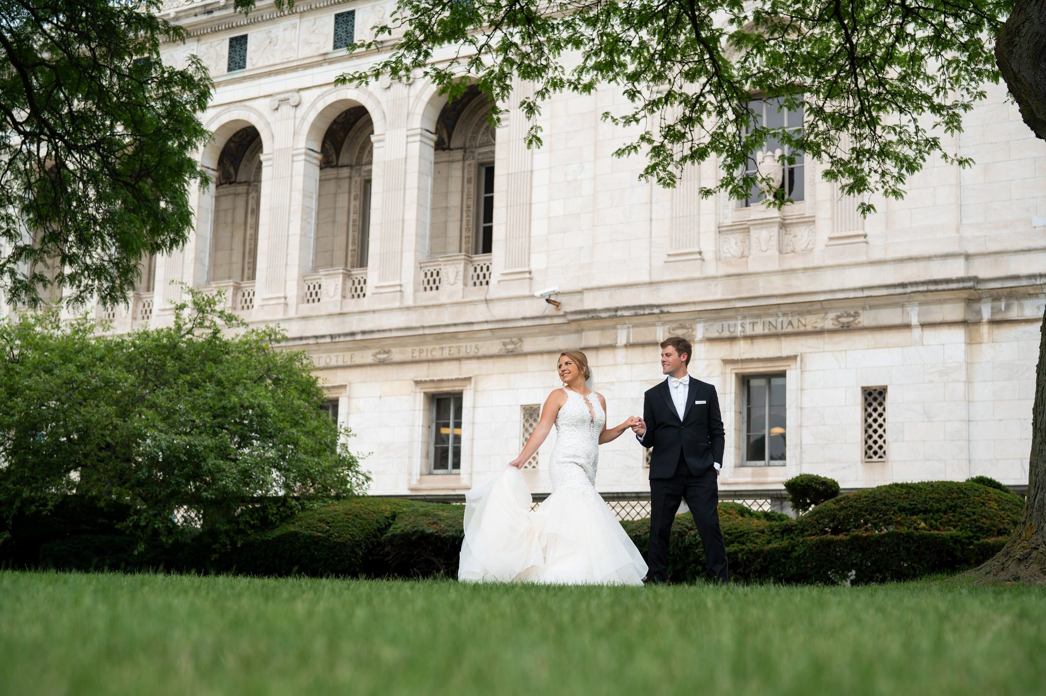 Newlyweds walk holding hands on the front lawn of the Detroit Public Library on their wedding day.  