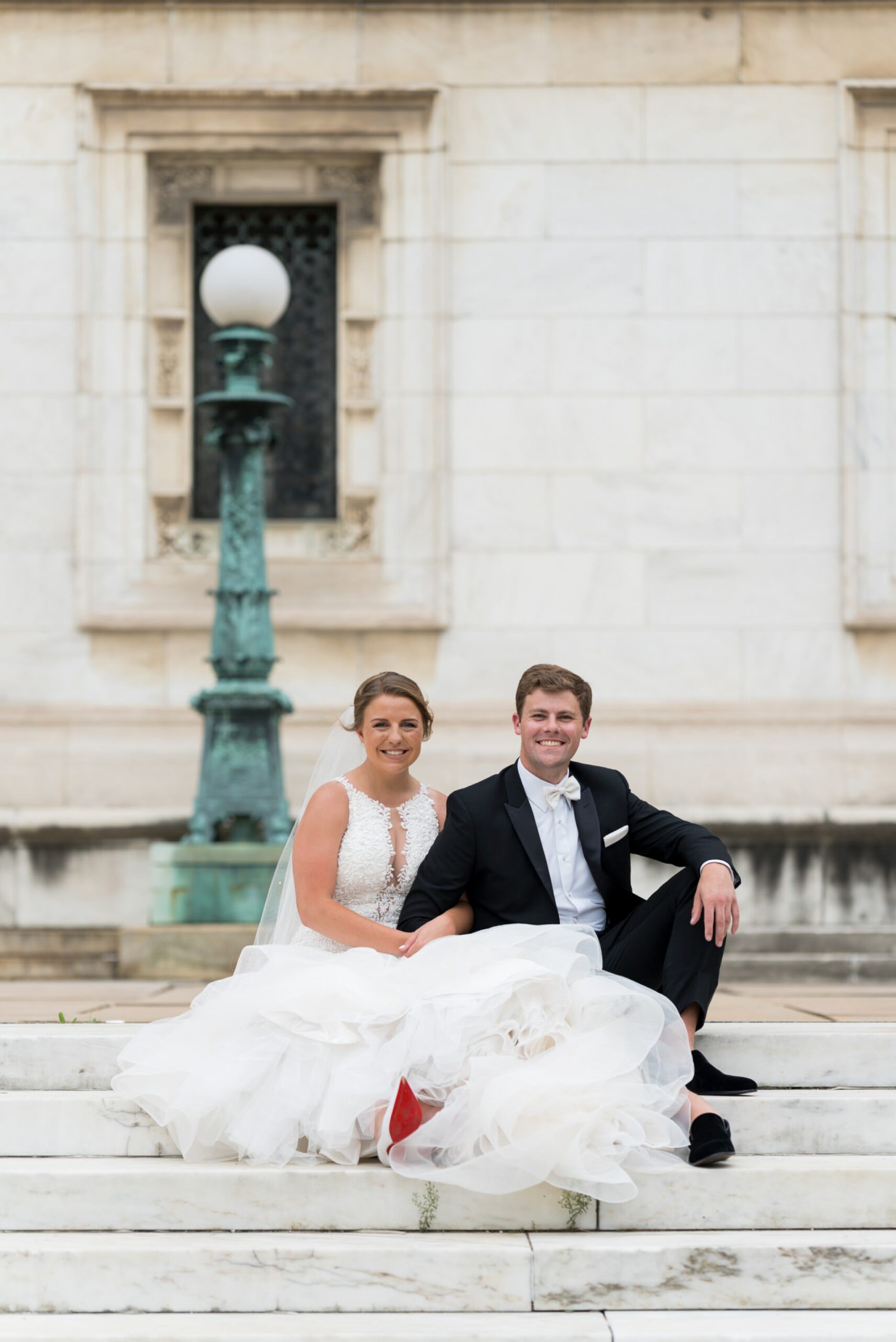 A bride and groom sit on the steps and pose for formals at Detroit Public LIbrary.