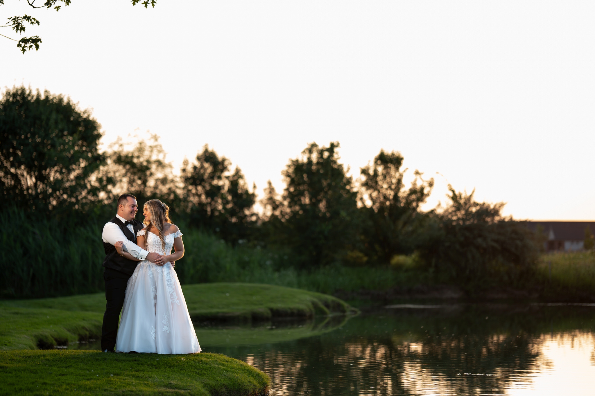 The bride and groom embrace near a lake during golden hour at a wedding reception at the Italian American Cultural Society. 