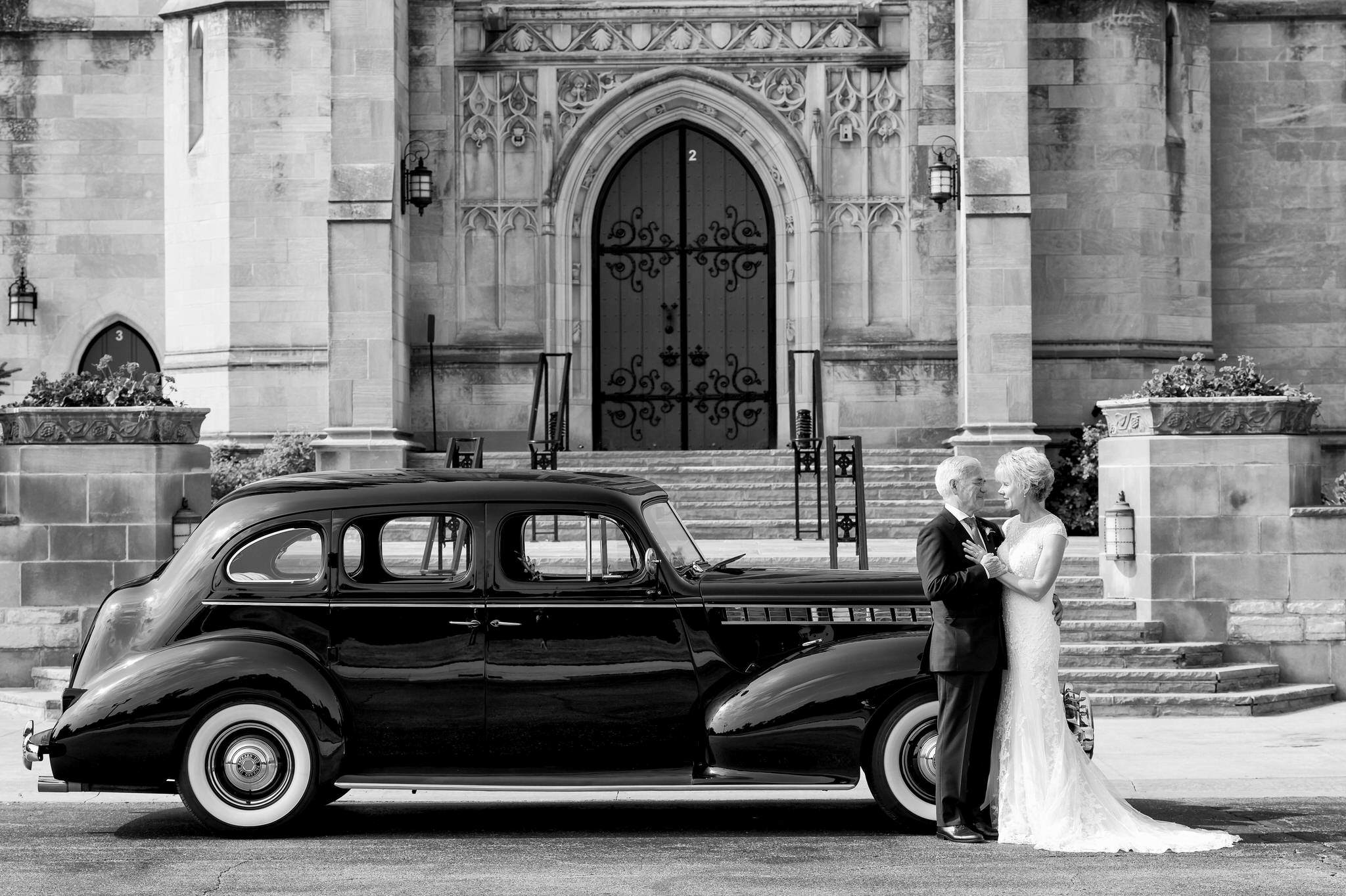 A bride and groom pose in front of a 1940 Packard from Motor City Vintage Rentals at their Kirk in the Hills wedding.