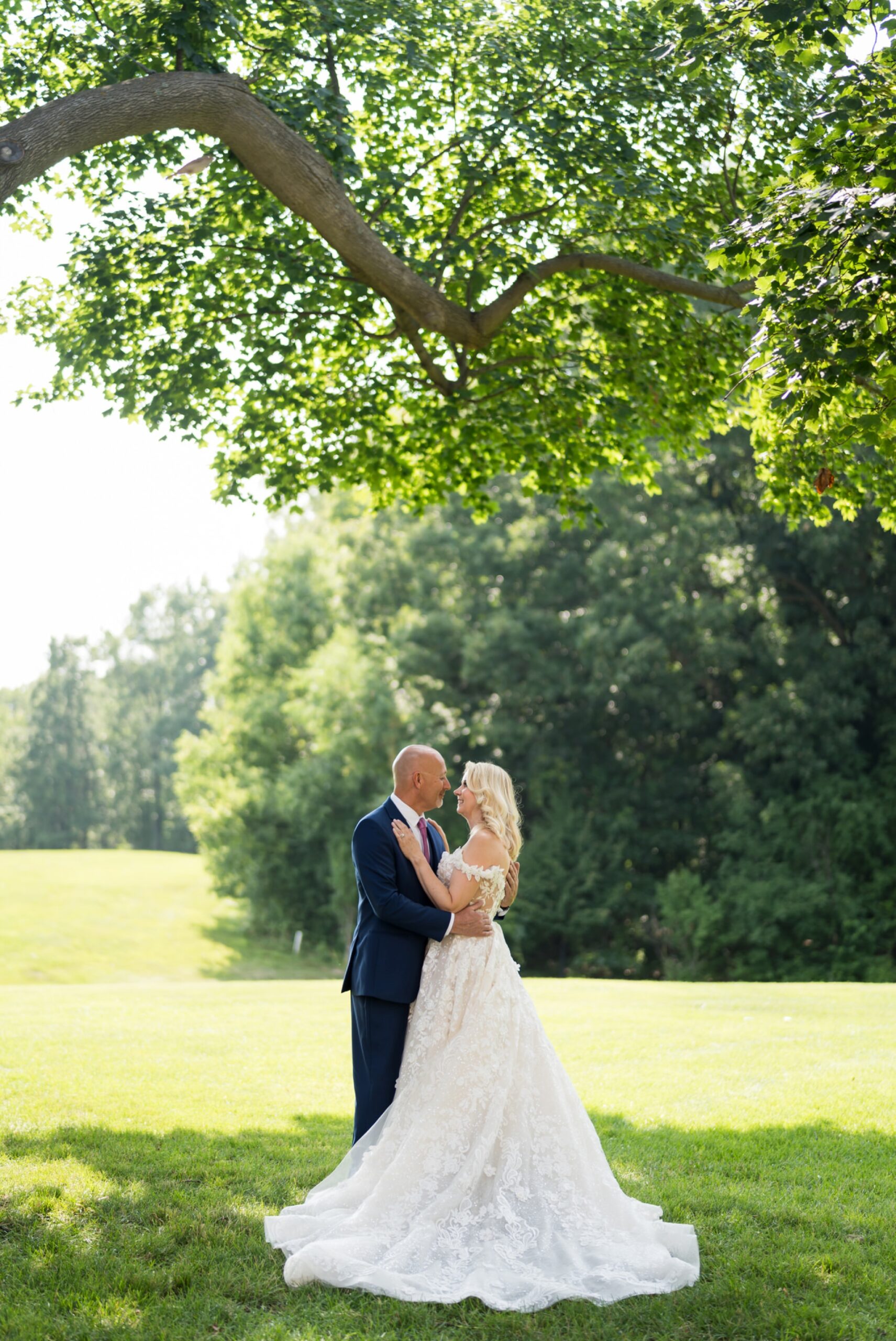 Standing under a tree, a bride and groom embrace on their wedding day at Meadow Brook Hall.  