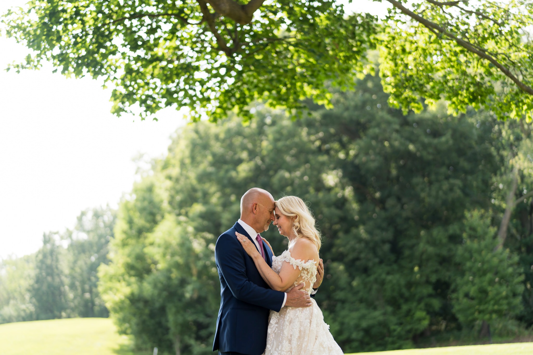 Standing under a tree, a bride and groom embrace on their wedding day at Meadow Brook Hall.  