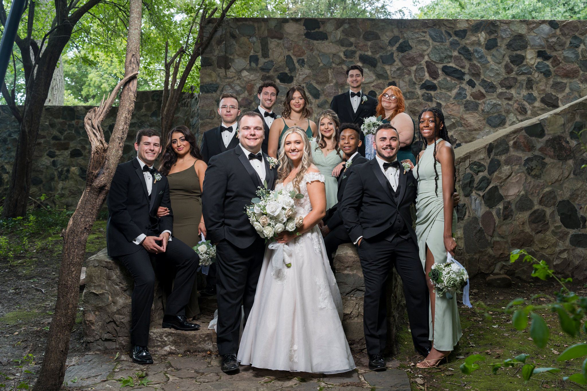 The bridal party poses for a formal photo along a stone wall at a Stony Creek wedding in Shelby Township, MI.   