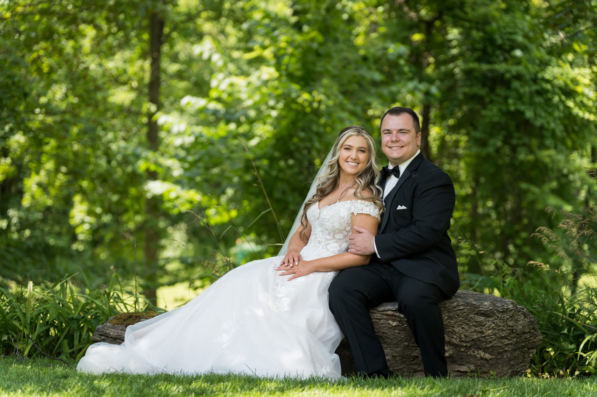 A bride and groom sit on a rock for a photo at Van Hoosen in Rochester, MI.  