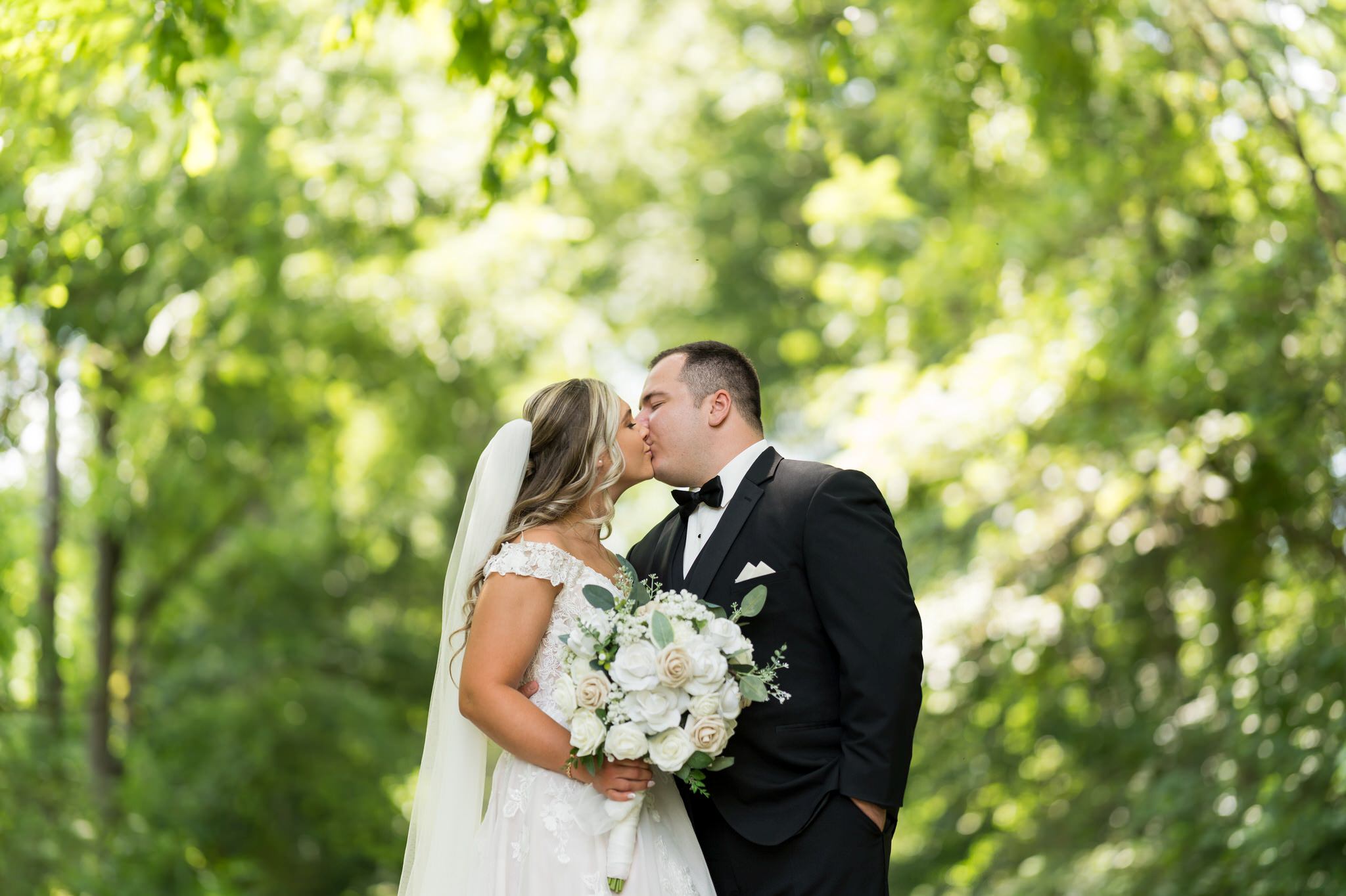 A bride and groom kiss among the trees at their Stony Creek wedding.  