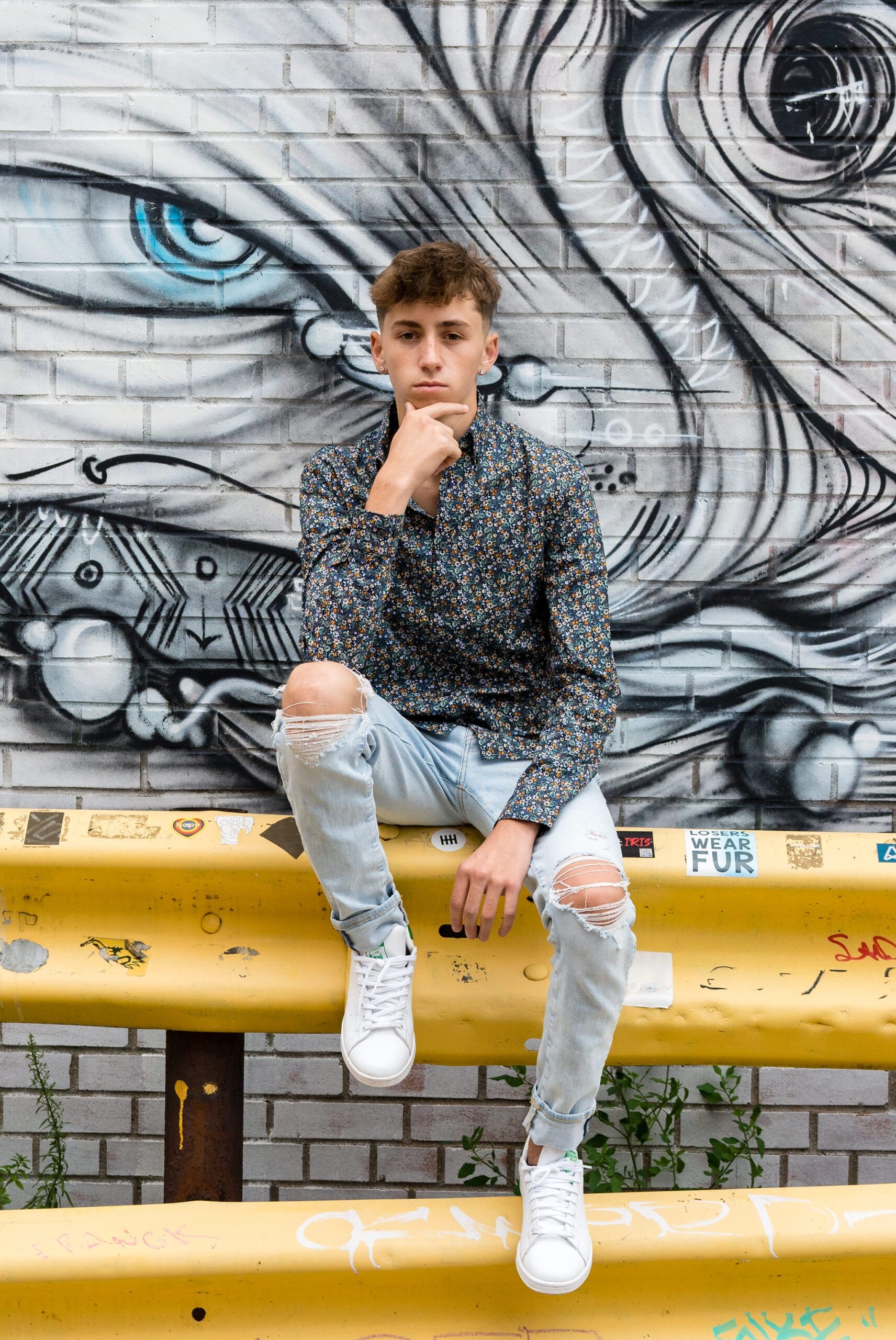 A male high school senior sits on a yellow railing for an Eastern Market senior photo  against a wall of graffiti.