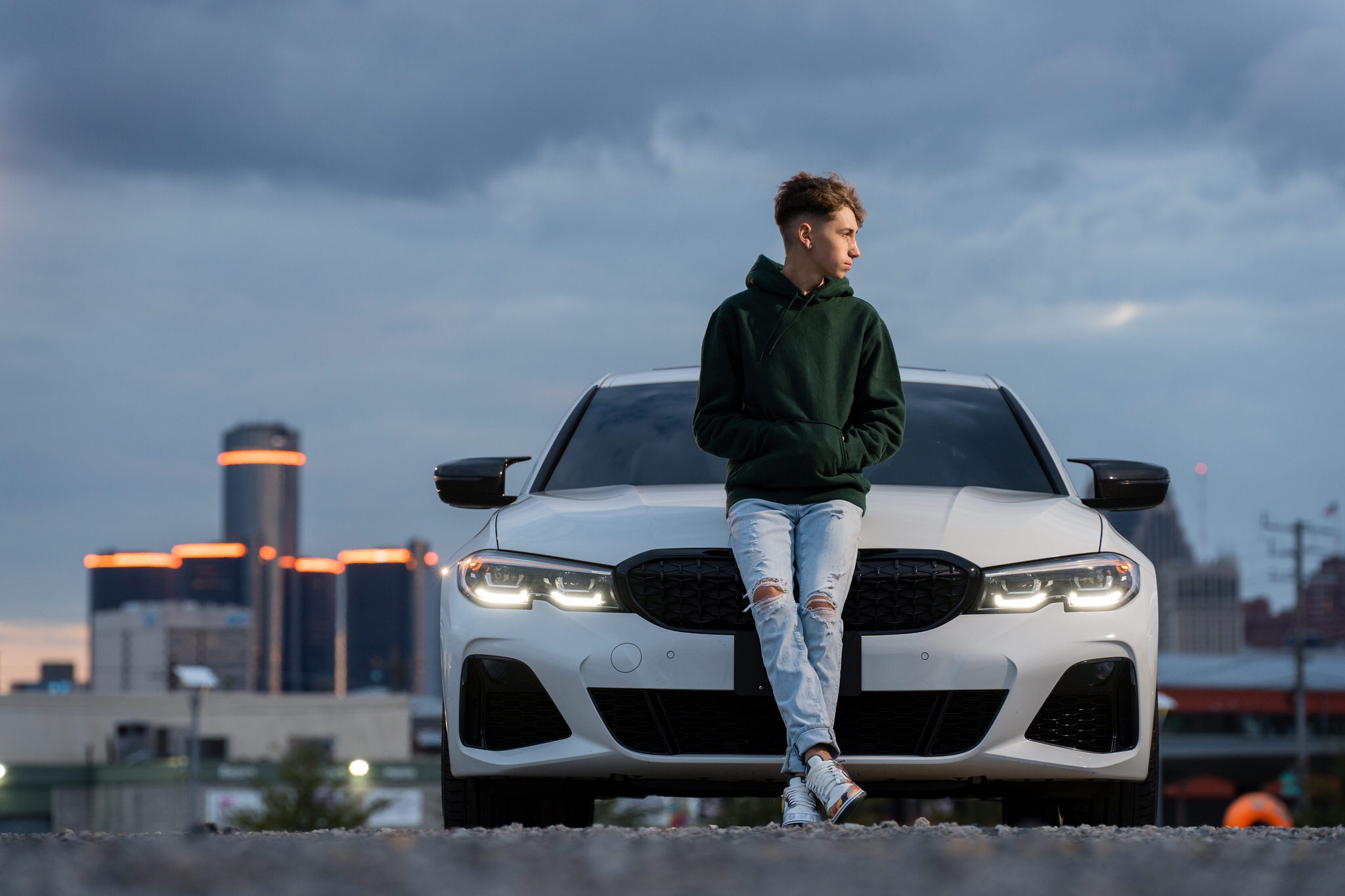 A guy wearing a green hoodie poses with a white BMW during his Eastern Market senior photos.   