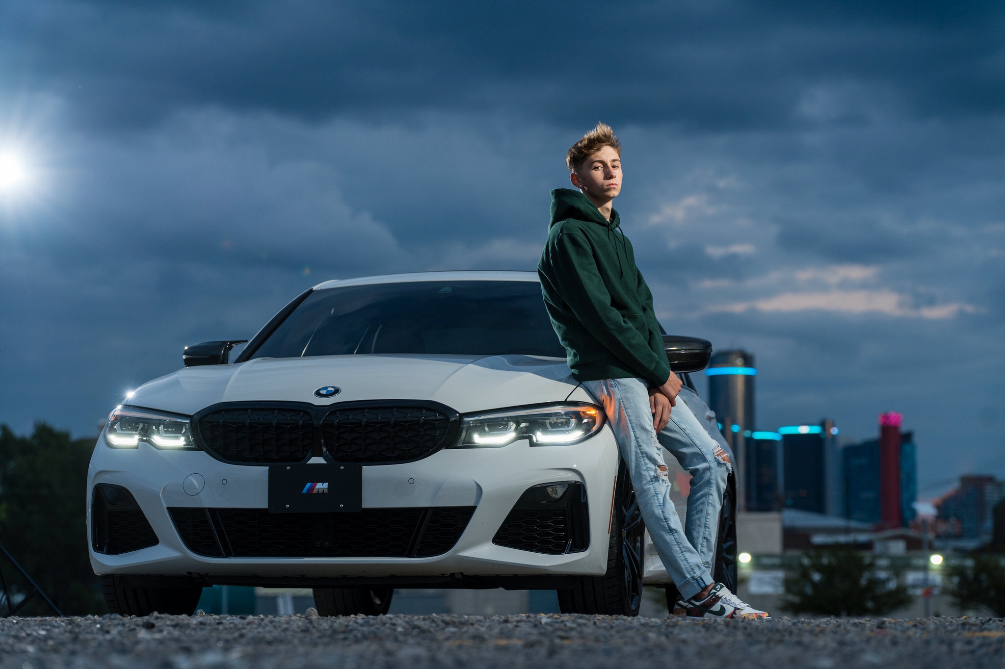 A guy wearing a green hoodie poses with a white BMW during his Eastern Market senior photos.   