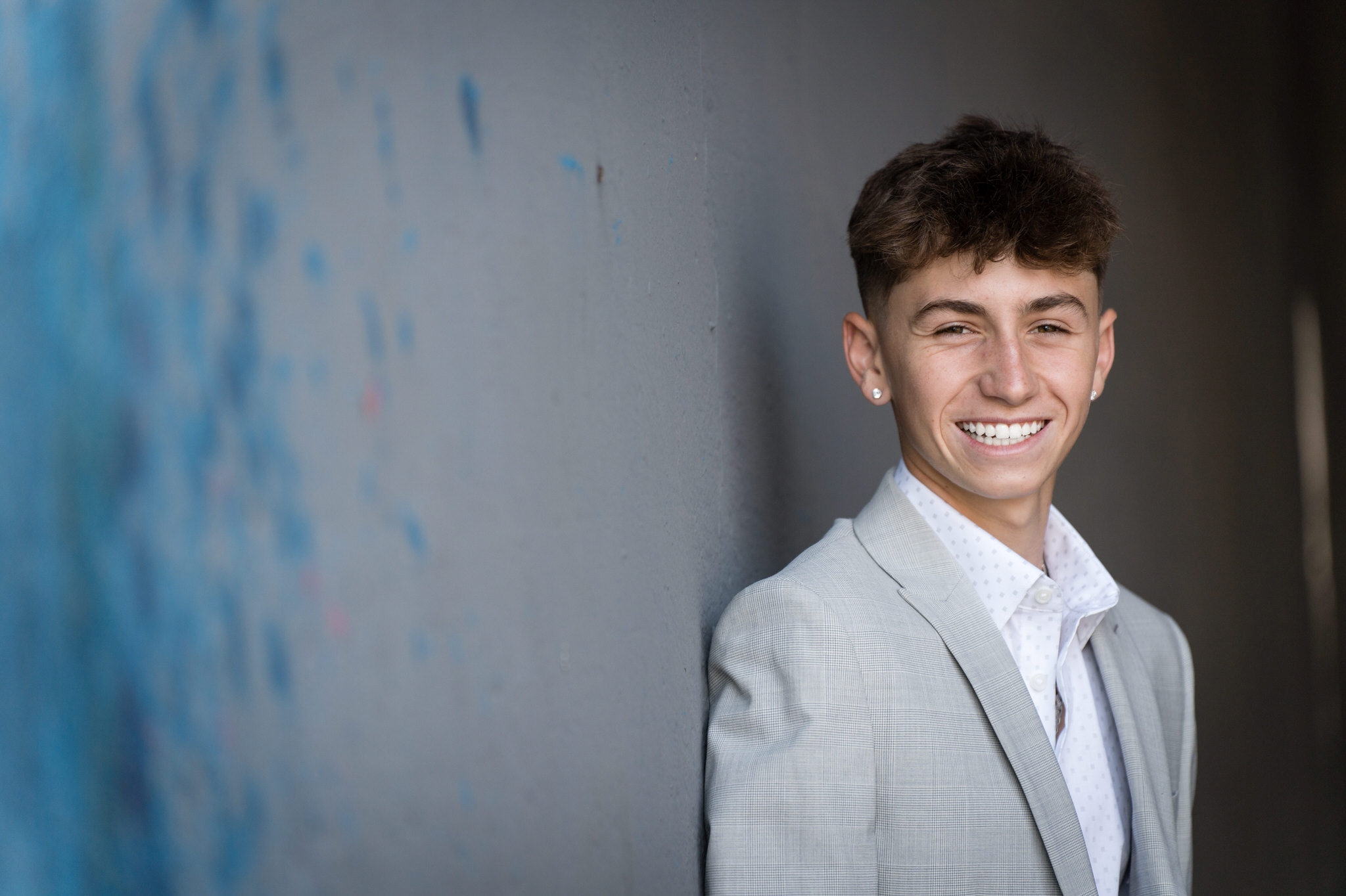 Male poses for a senior photo in Detroit against a grey and blue wall.  