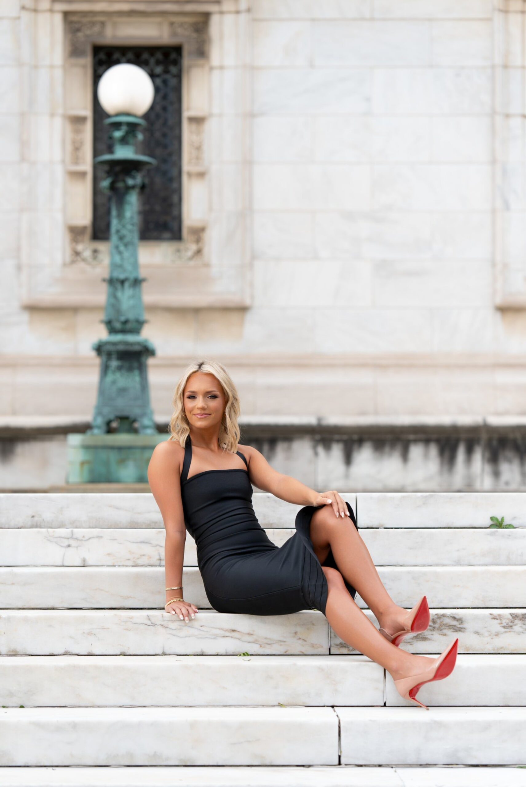 A female high school senior wearing a black dress and Christian Louboutin heels poses for her Detroit senior photos at the Detroit Public Library.