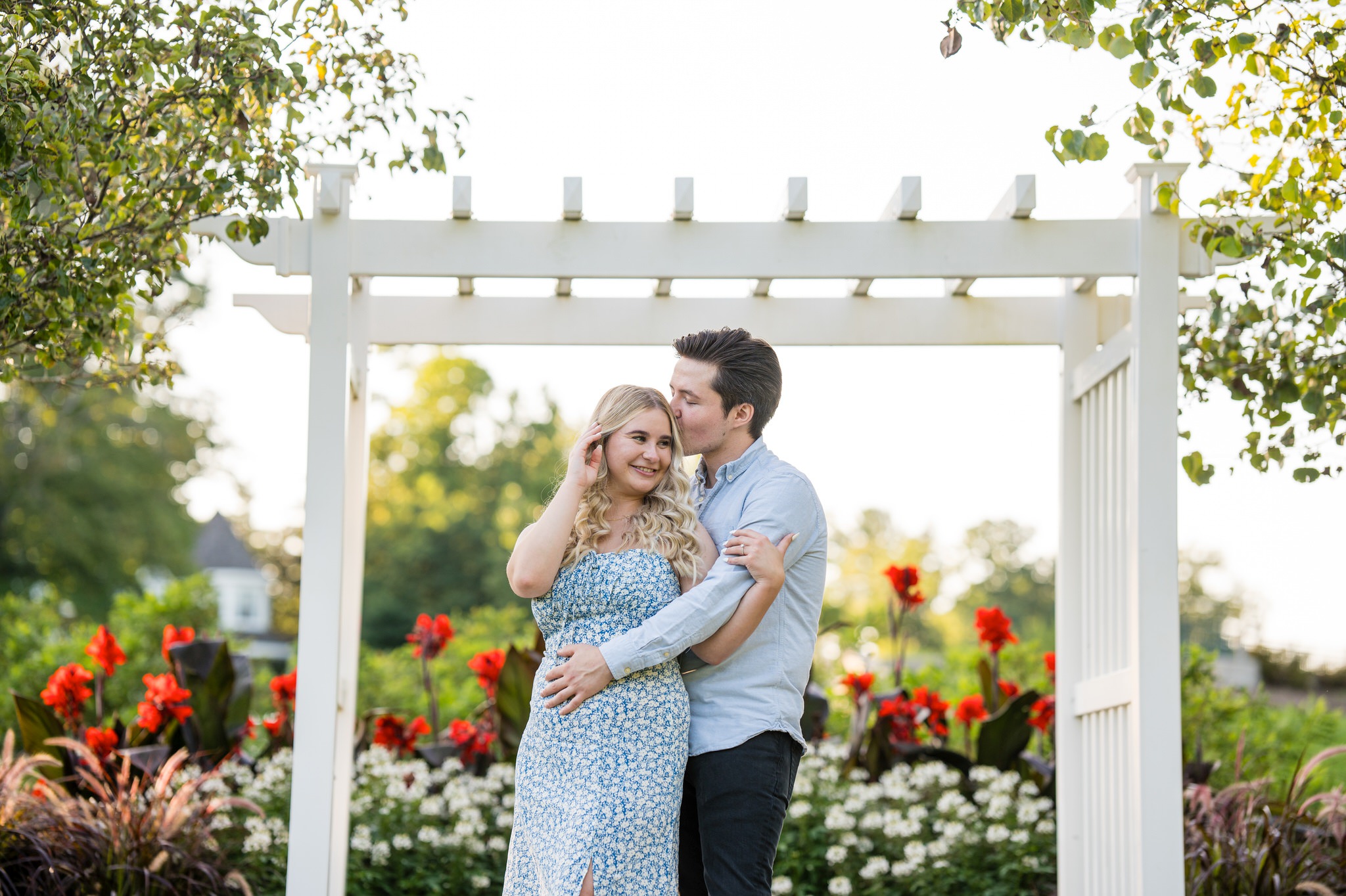 A guy kisses his fiance on the temple under a white trellis at their Quarton Lake proposal. 