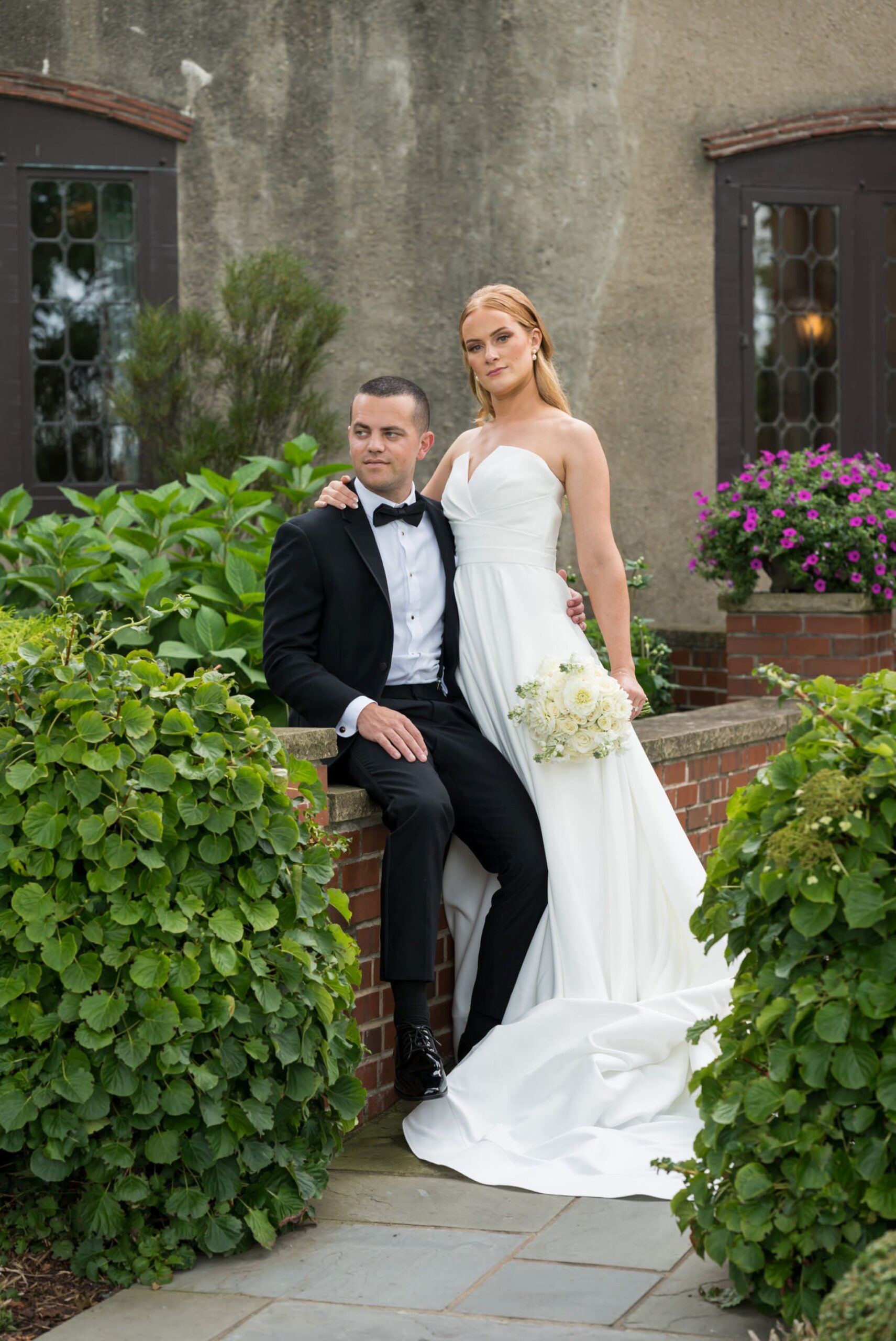 A bride and groom pose on a brick wall at their Country Club of Detroit wedding.  