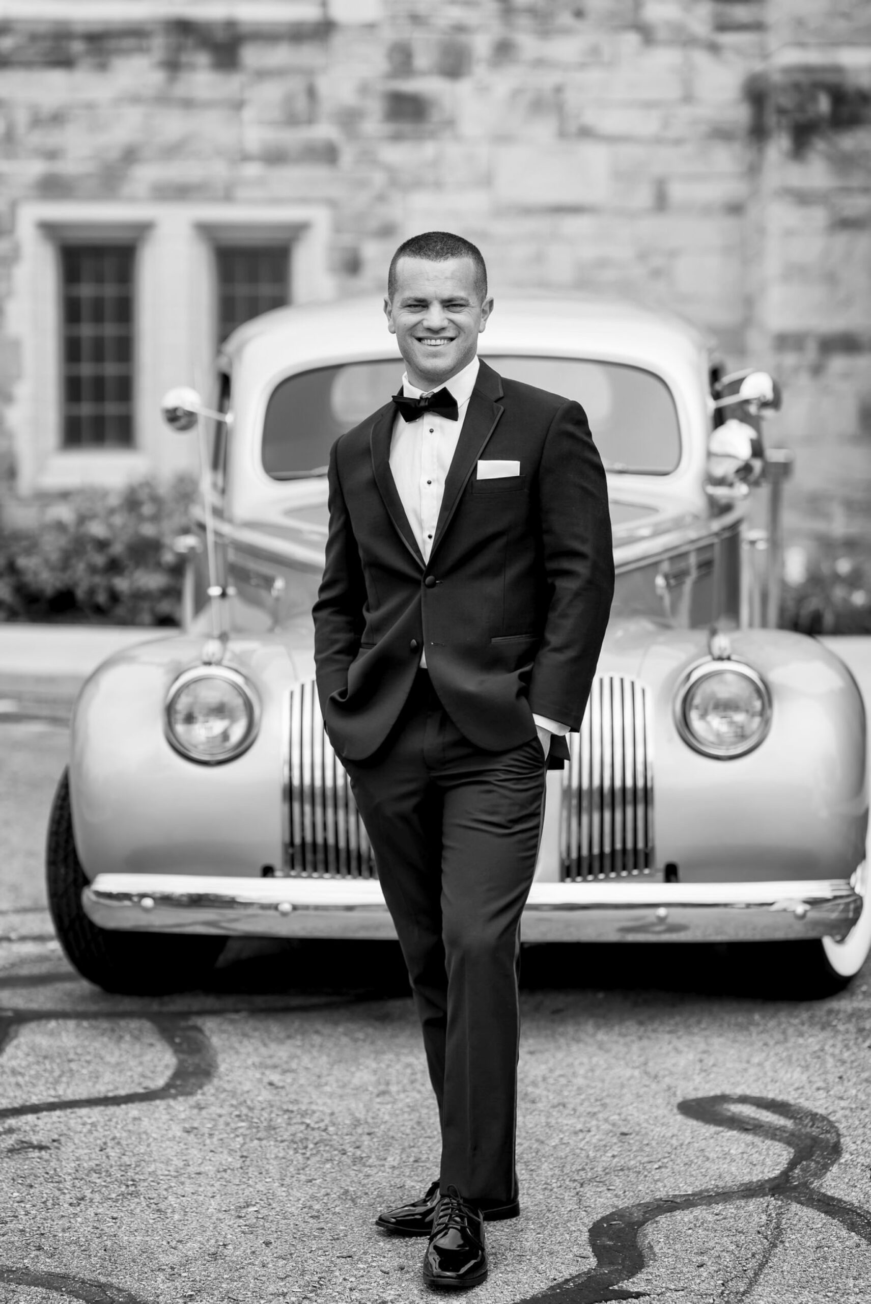 A groom poses in front of a classic Packard from Motor City Vintage Rentals.  