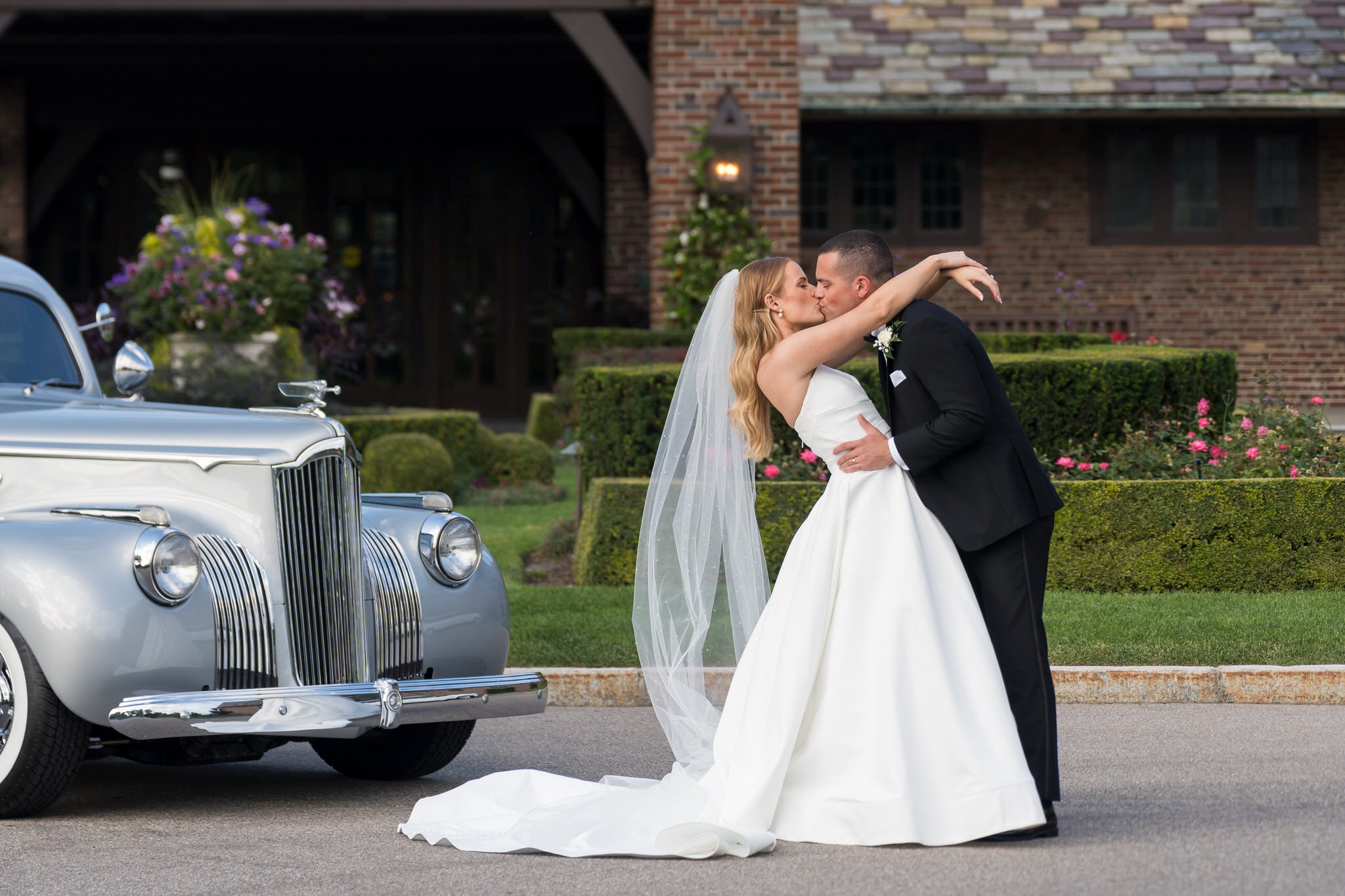A bride and groom pose outside of their Country Club of Detroit wedding reception with an antique Packard car from Motor City Vintage Rentals.