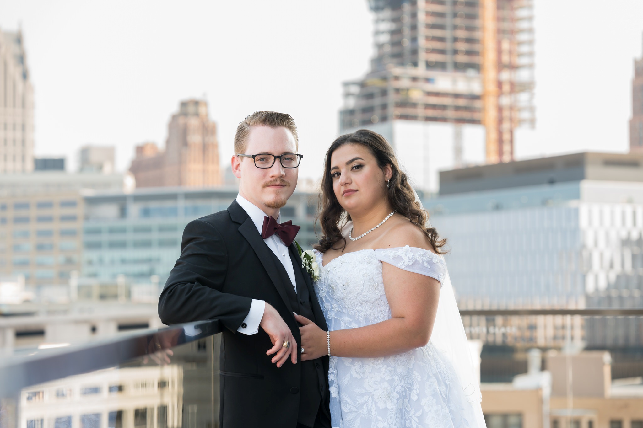 A couple embraces with the Detroit city skyline behind them at their Detroit Athletic Club wedding.  