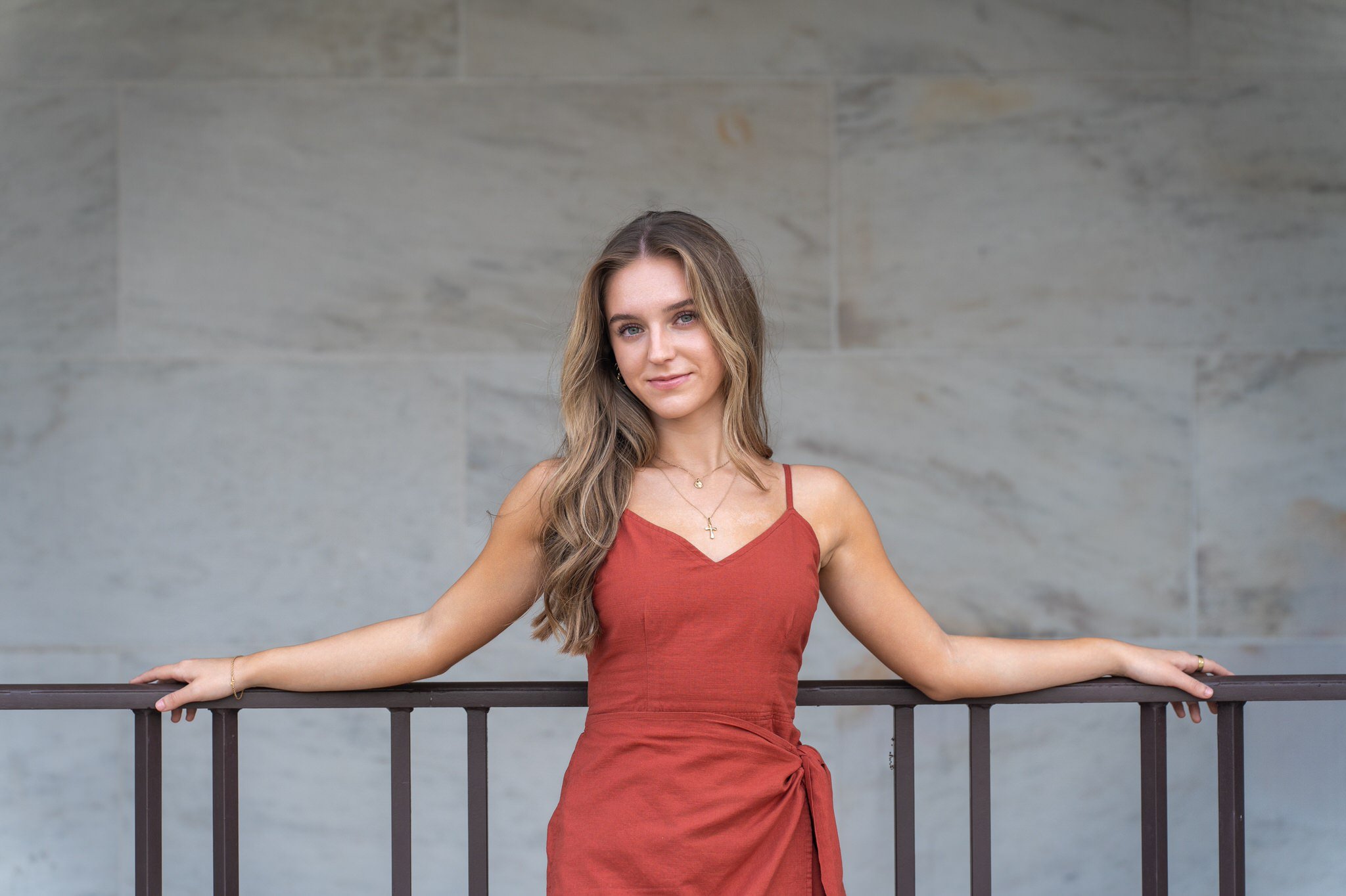 A teen girl wearing a red dress poses using a railing during her DIA senior photos. 