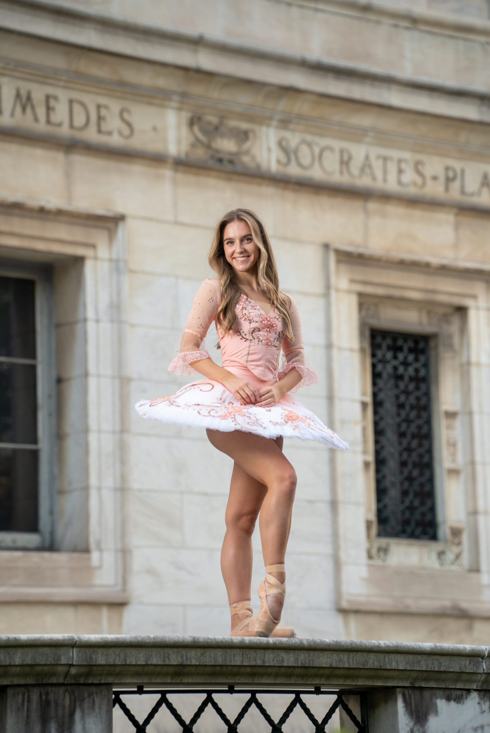 A ballerina, wearing a pink tutu, poses on top of a wall in Detroit during her senior photos.