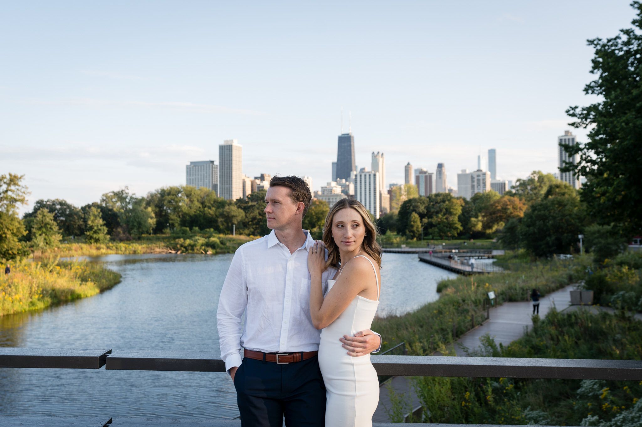A couple poses, looking in opposite directions, with the skyline in the background of their Lincoln Park Chicago engagement session. 